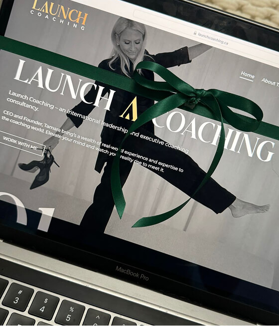 Laptop screen showing Launch Coaching website homepage with a woman holding shoes and a dark green ribbon bow overlay.