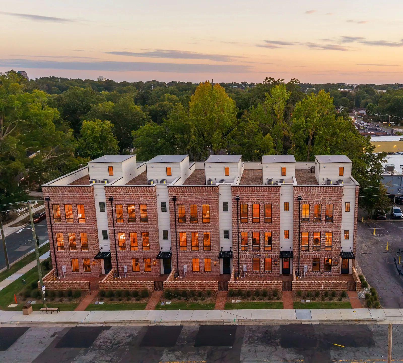 Twilight aerial of contemporary brick townhomes with illuminated interiors in Durham, North Carolina.