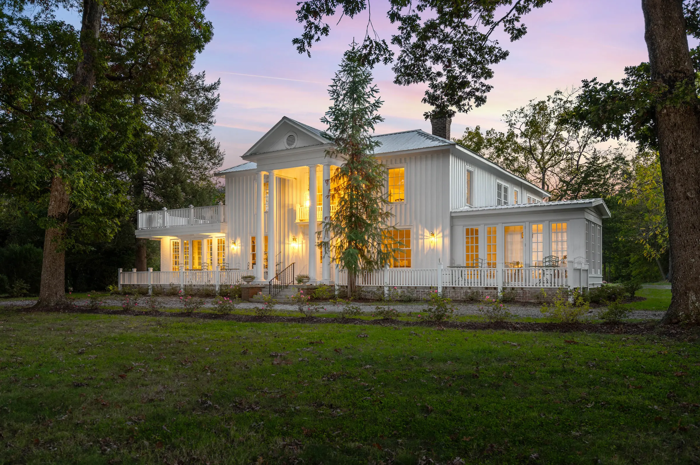 White columned Mebane home with warmly lit windows and a broad front porch at twilight, photographed by Upper Echelon Visuals