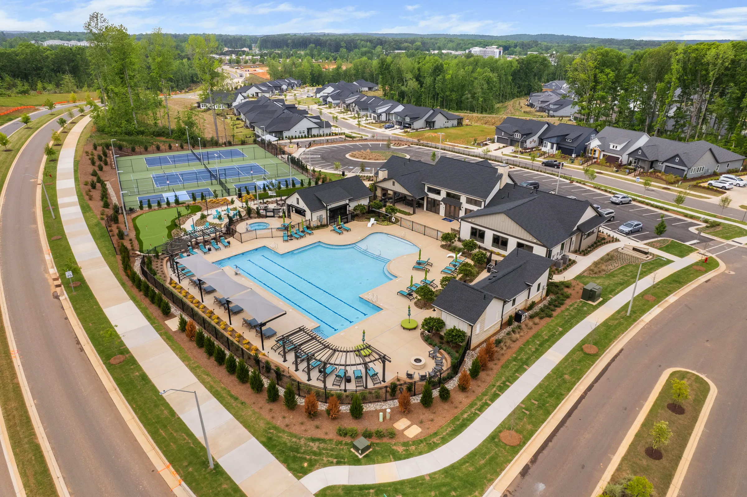 Aerial view of a Pittsboro community pool, clubhouse, and courts surrounded by homes and trees by Upper Echelon Visuals