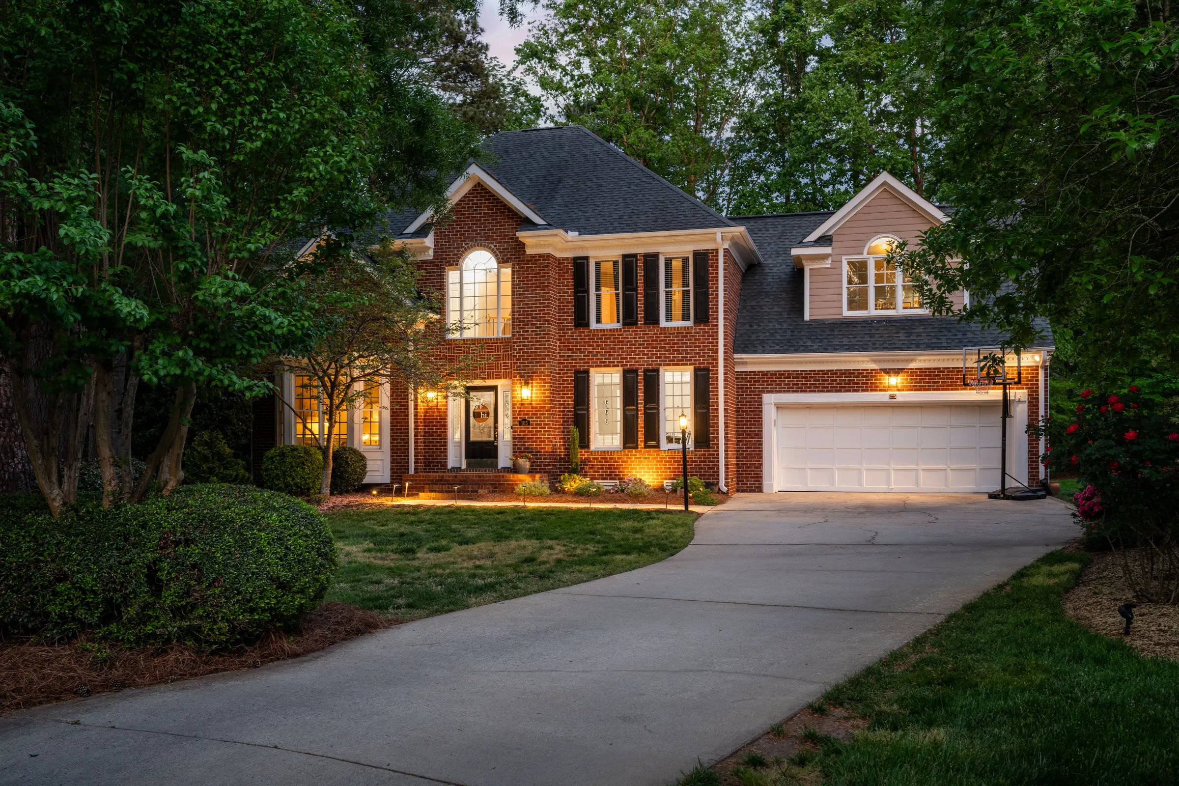 Two-story brick Smithfield home with black shutters and warmly lit windows at dusk, photographed by Upper Echelon Visuals