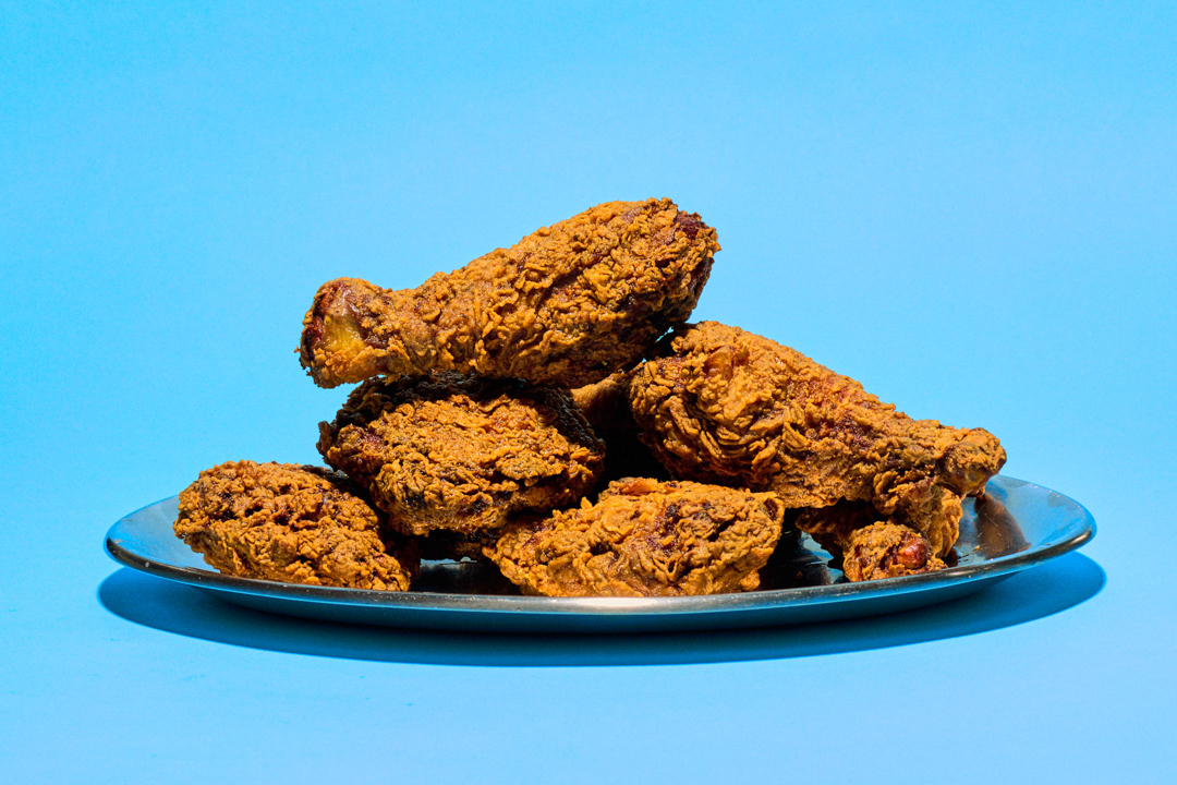 Plate stacked with crispy fried chicken drumsticks and pieces on a blue background.
