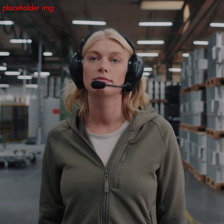 Kvinna med headset och mikrofon bär en grågrön fleecejacka i ett lagerlokal.