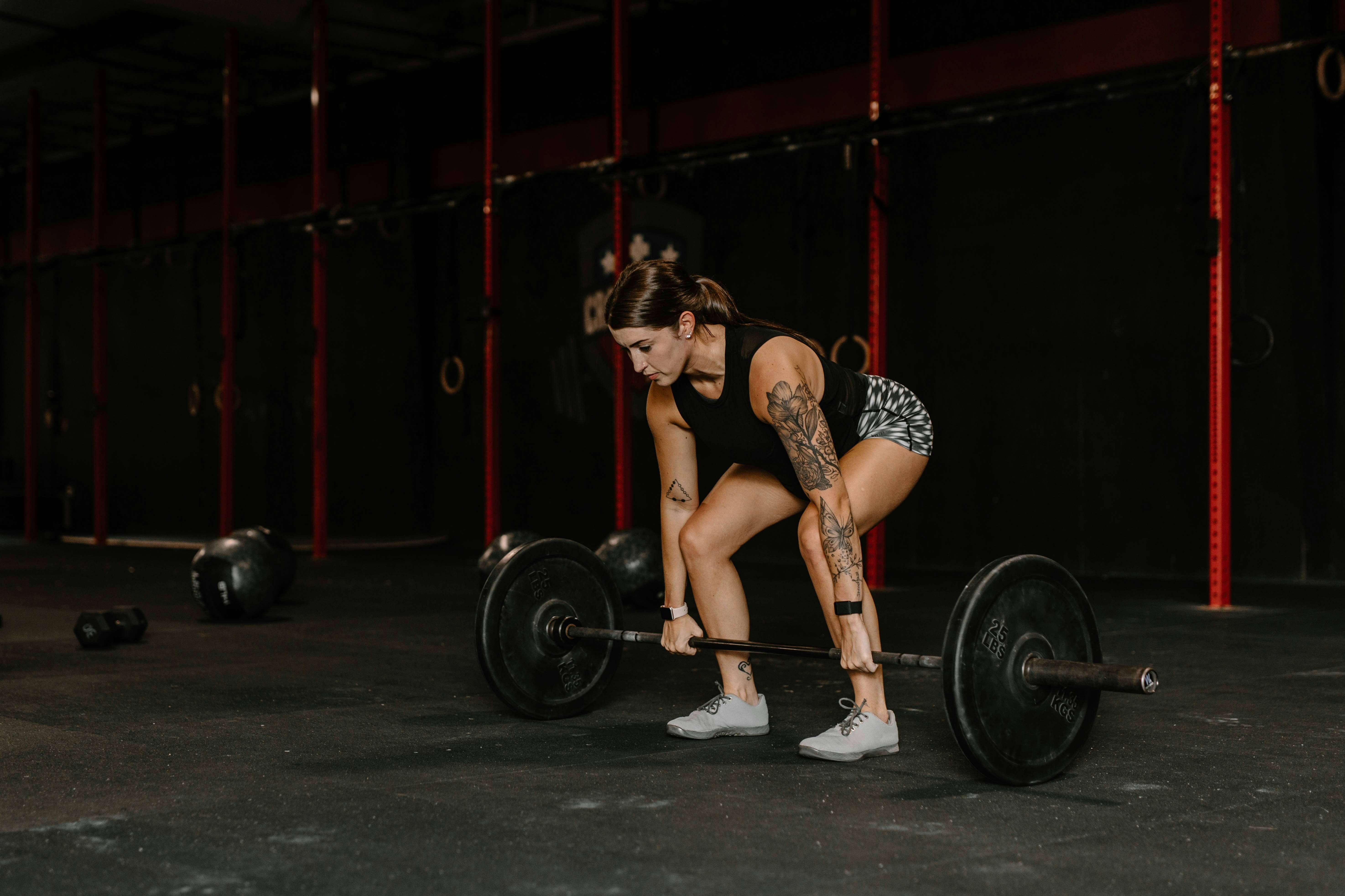 Woman lifting a barbell in a gym, showing how high activity levels can impact how long lip filler lasts