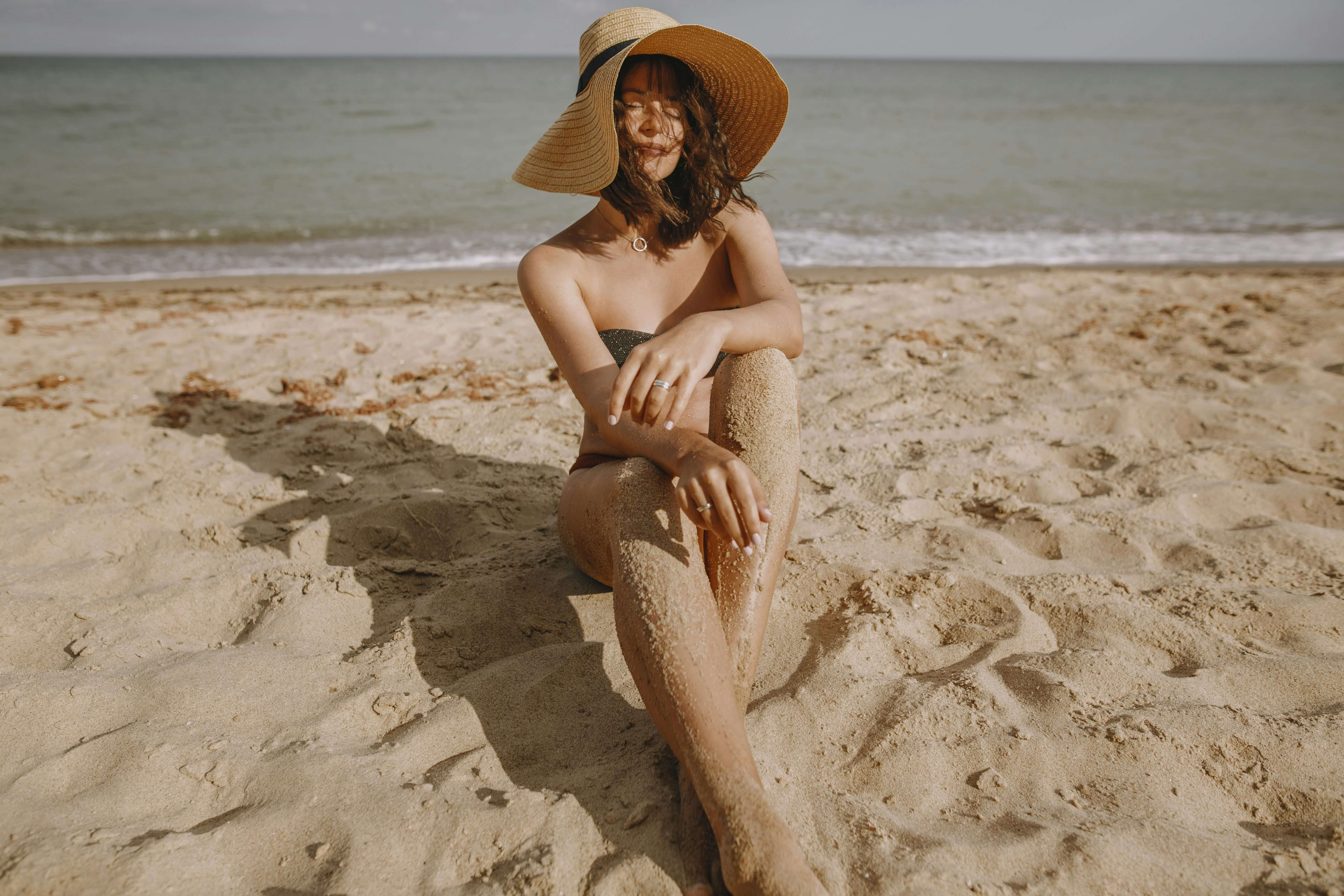 Woman sitting on a sunny beach, representing how UV exposure can break down lip filler over time