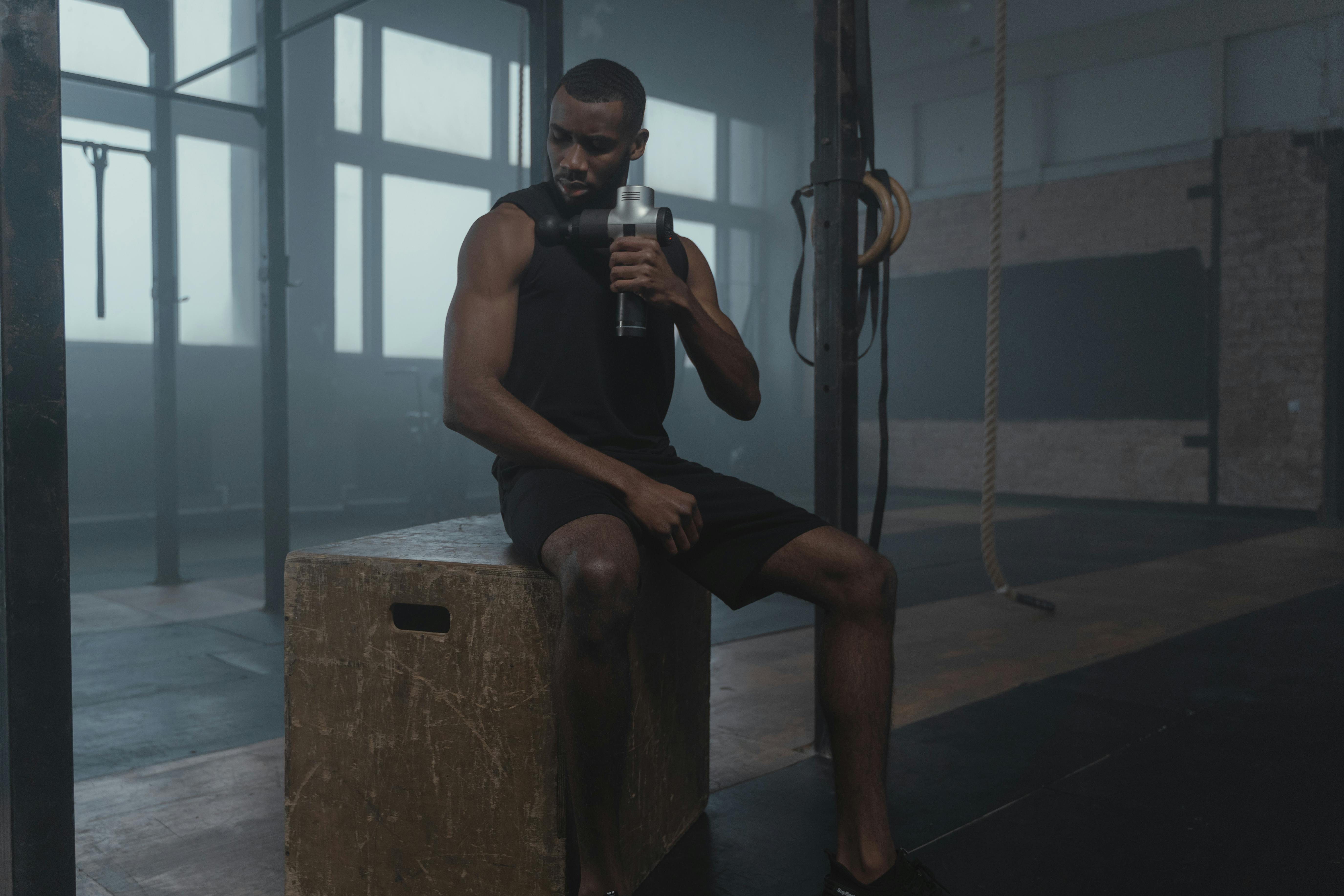 Fit man using massage gun on shoulder for muscle recovery and peptide therapy healing