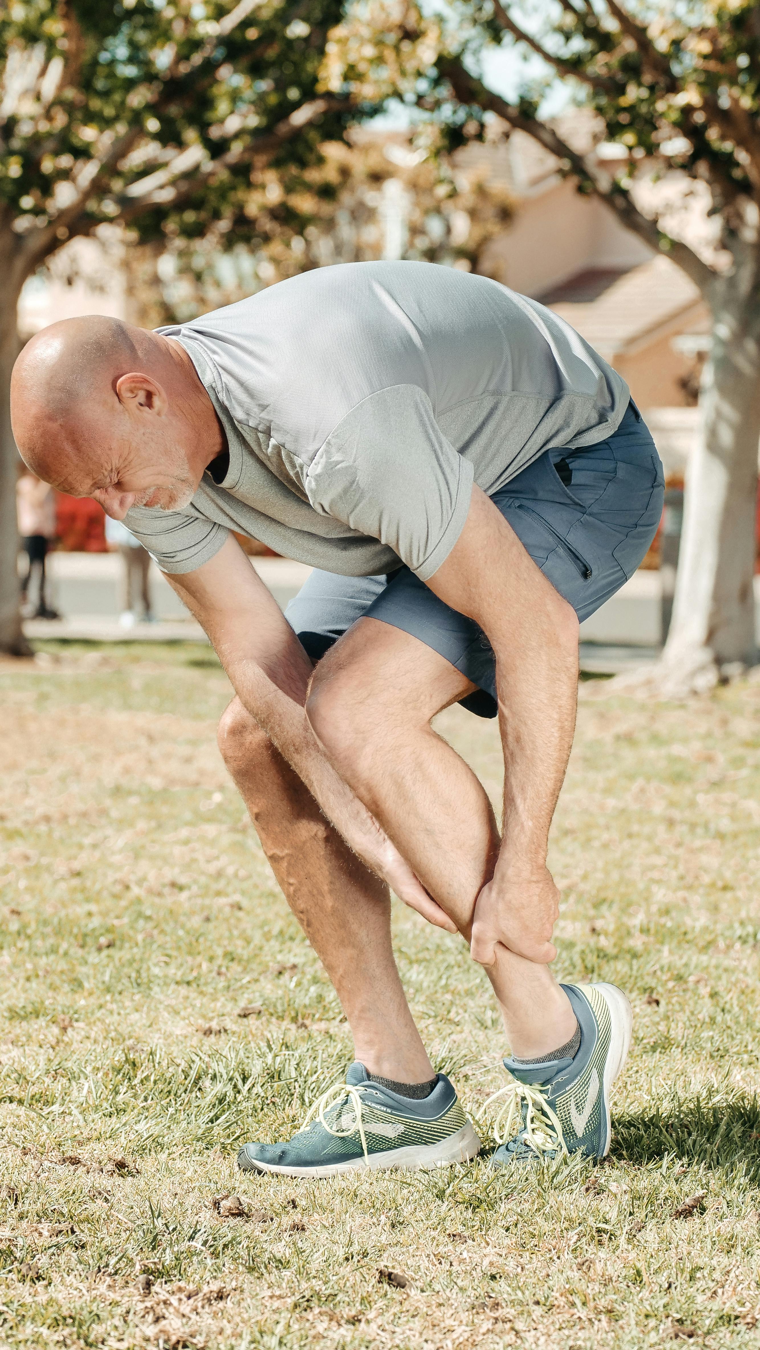 Man holding ankle in discomfort after running in a park, illustrating sports injury recovery and BPC-157 peptide healing