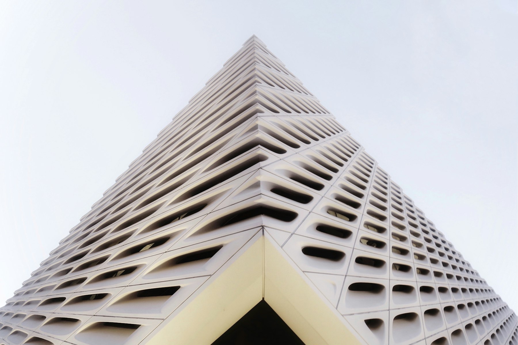 Corner of a white honeycomb facade rising into a pale sky