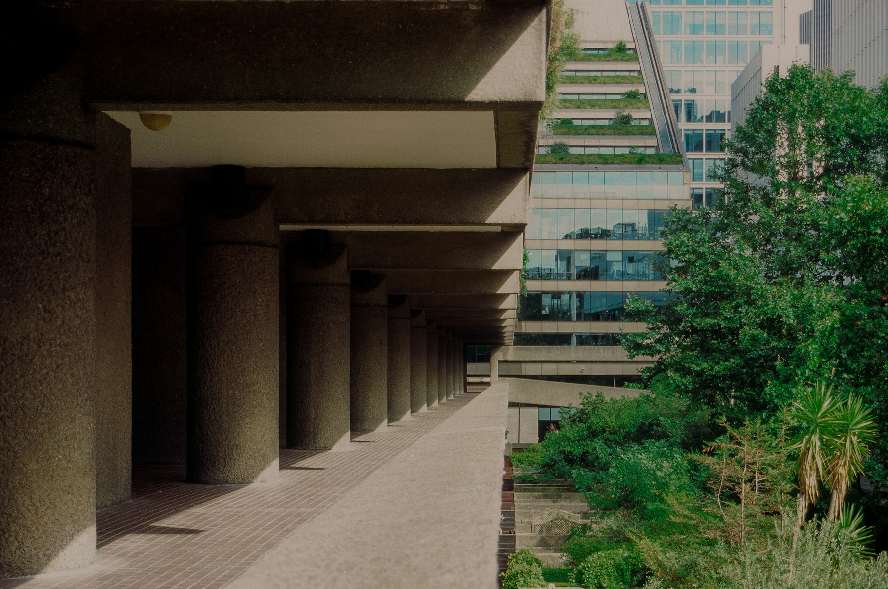 Concrete colonnade beside planted terraces and a stepped glass building