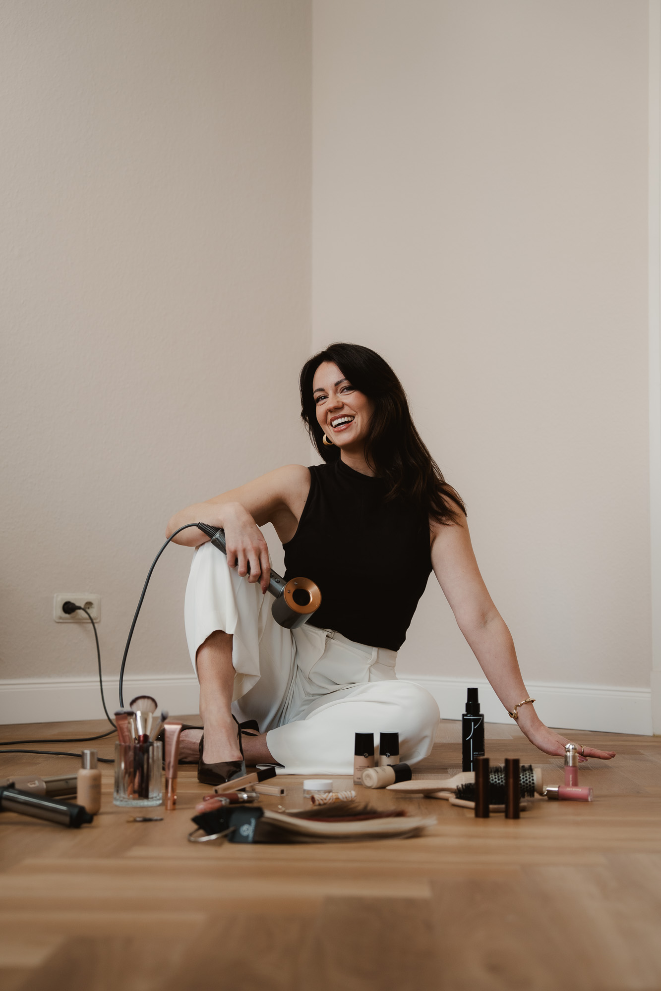 Woman sitting on the floor surrounded by hairstyling tools and products.