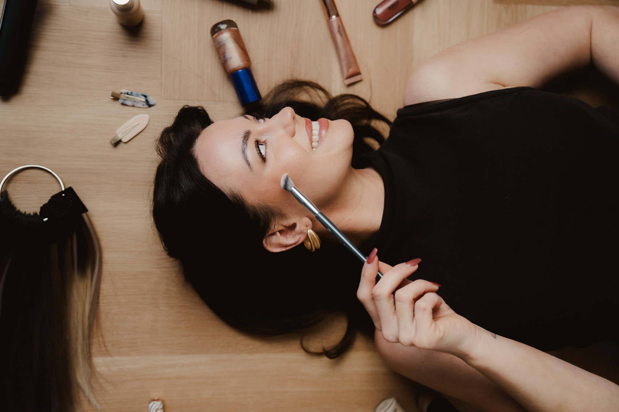 Woman lying on the floor surrounded by hairstyling tools and beauty products.