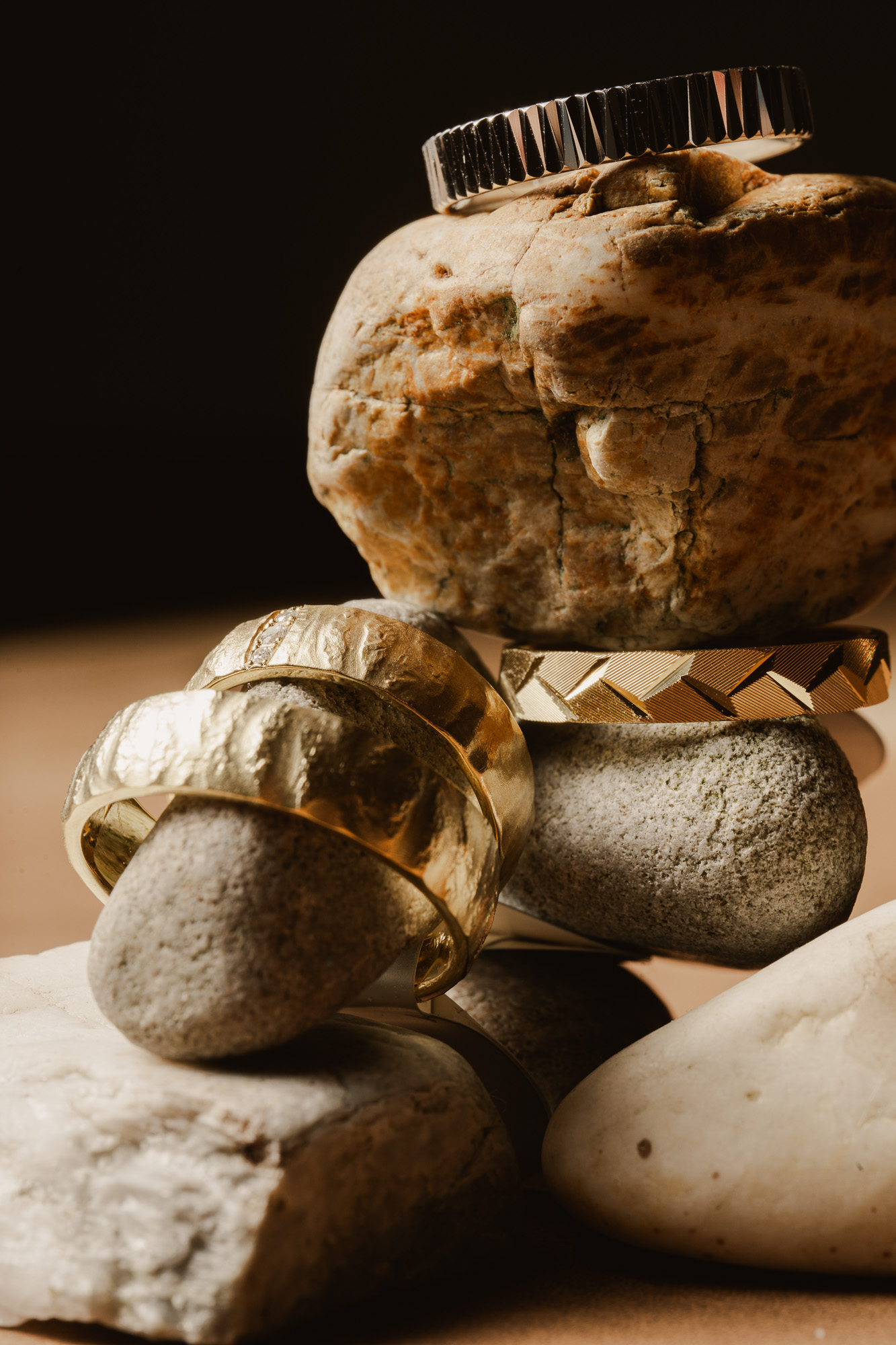 Different wedding rings stated around and on solid rocks in warm directional light.