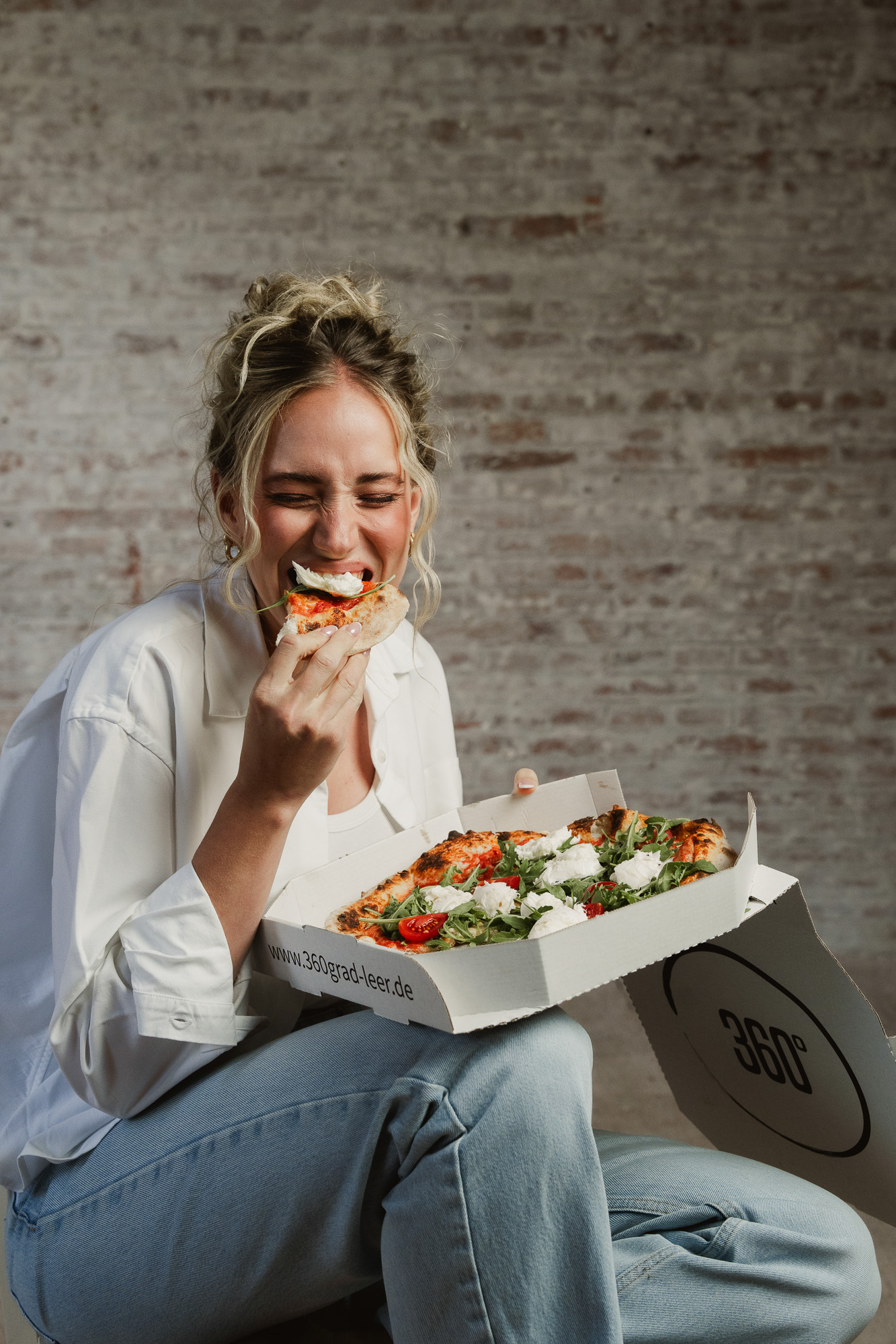 Woman sitting casually with an open pizza box and a slice of pizza.