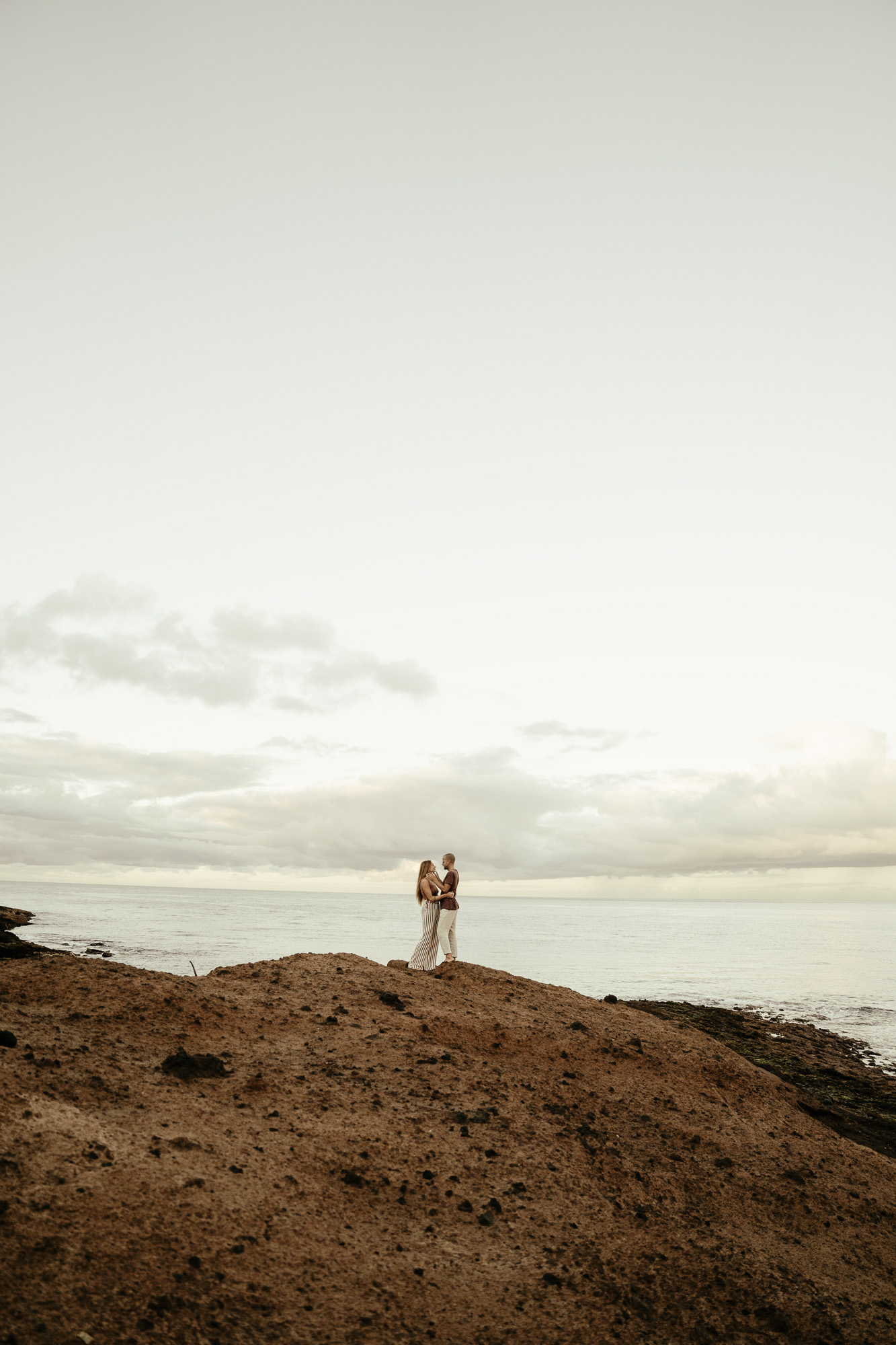 Couple standing together on a remote coastal landscape beneath a wide sky.