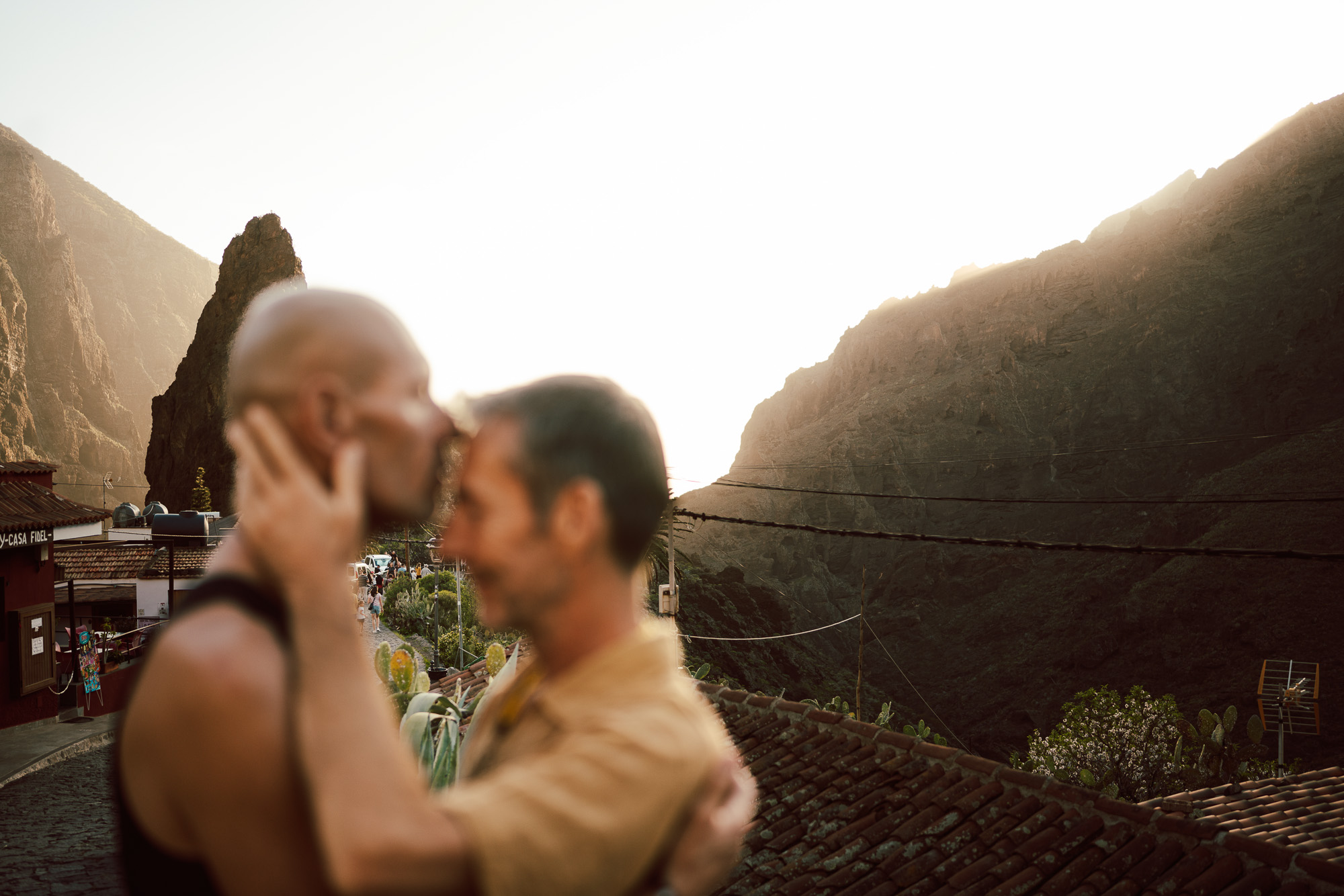 Couple touching faces in warm backlight between dramatic mountain slopes.