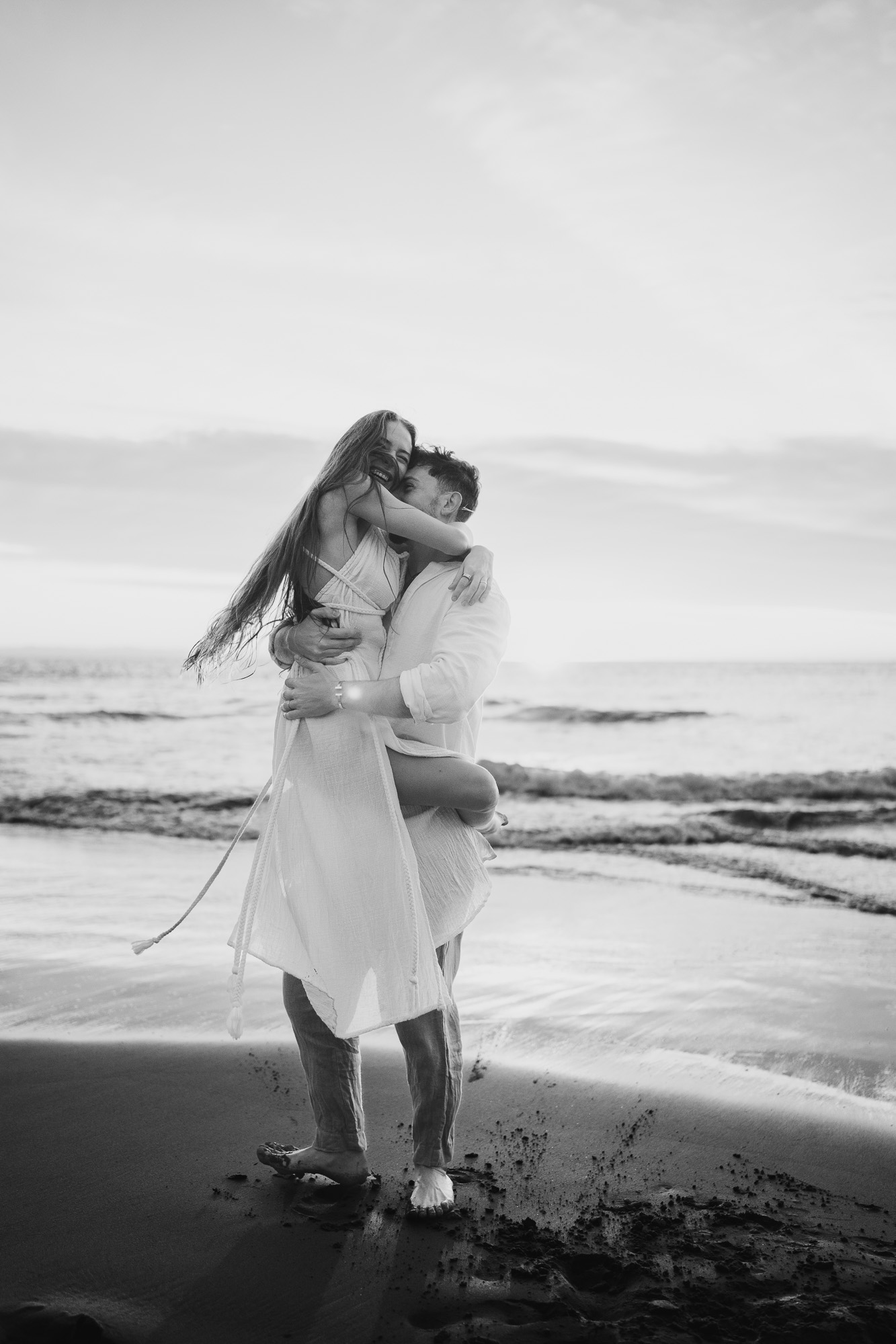 Black-and-white photograph of a couple embracing at the edge of the sea.