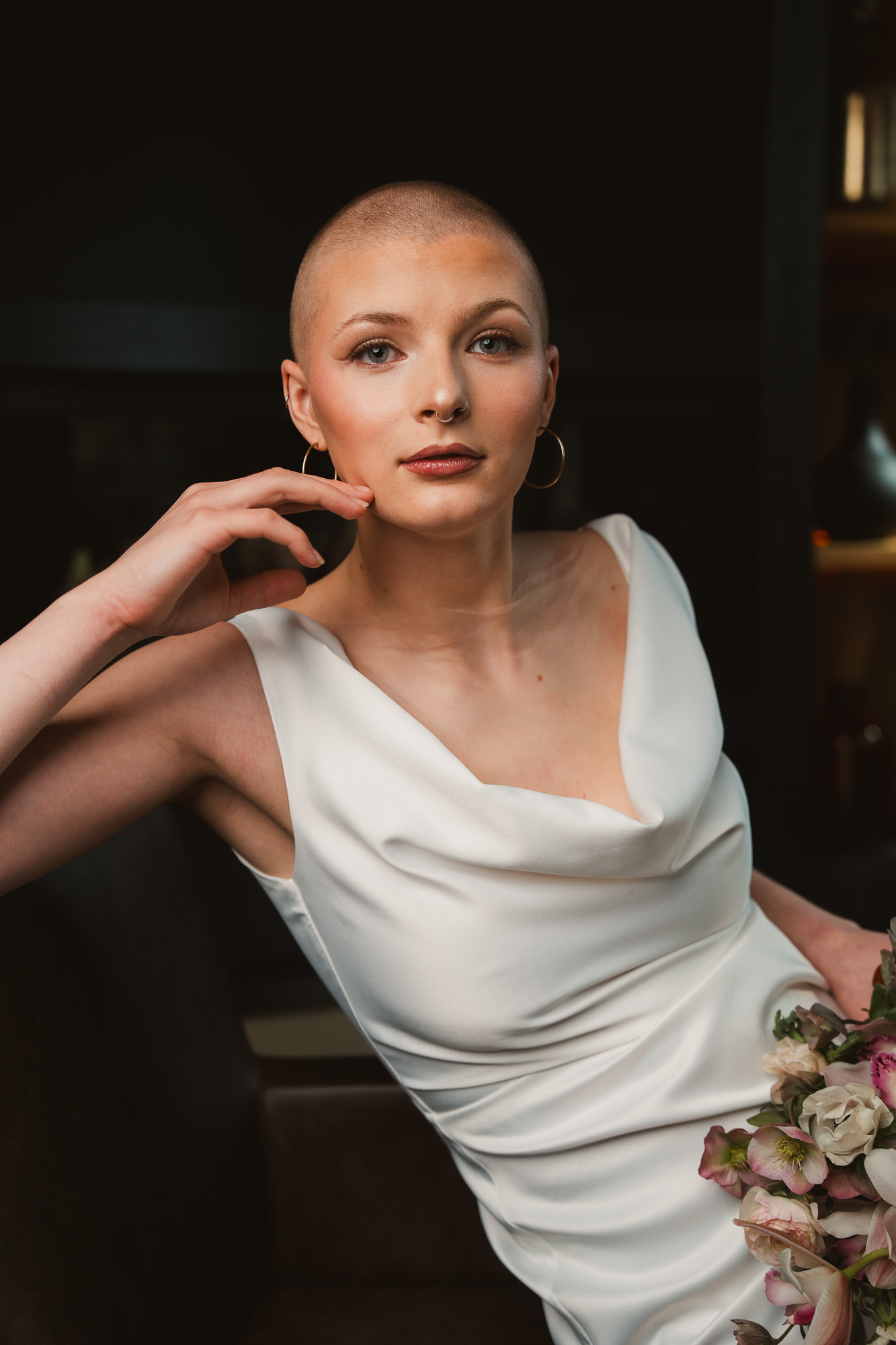 Editorial portrait of a woman in a white dress resting her hand beside her face.