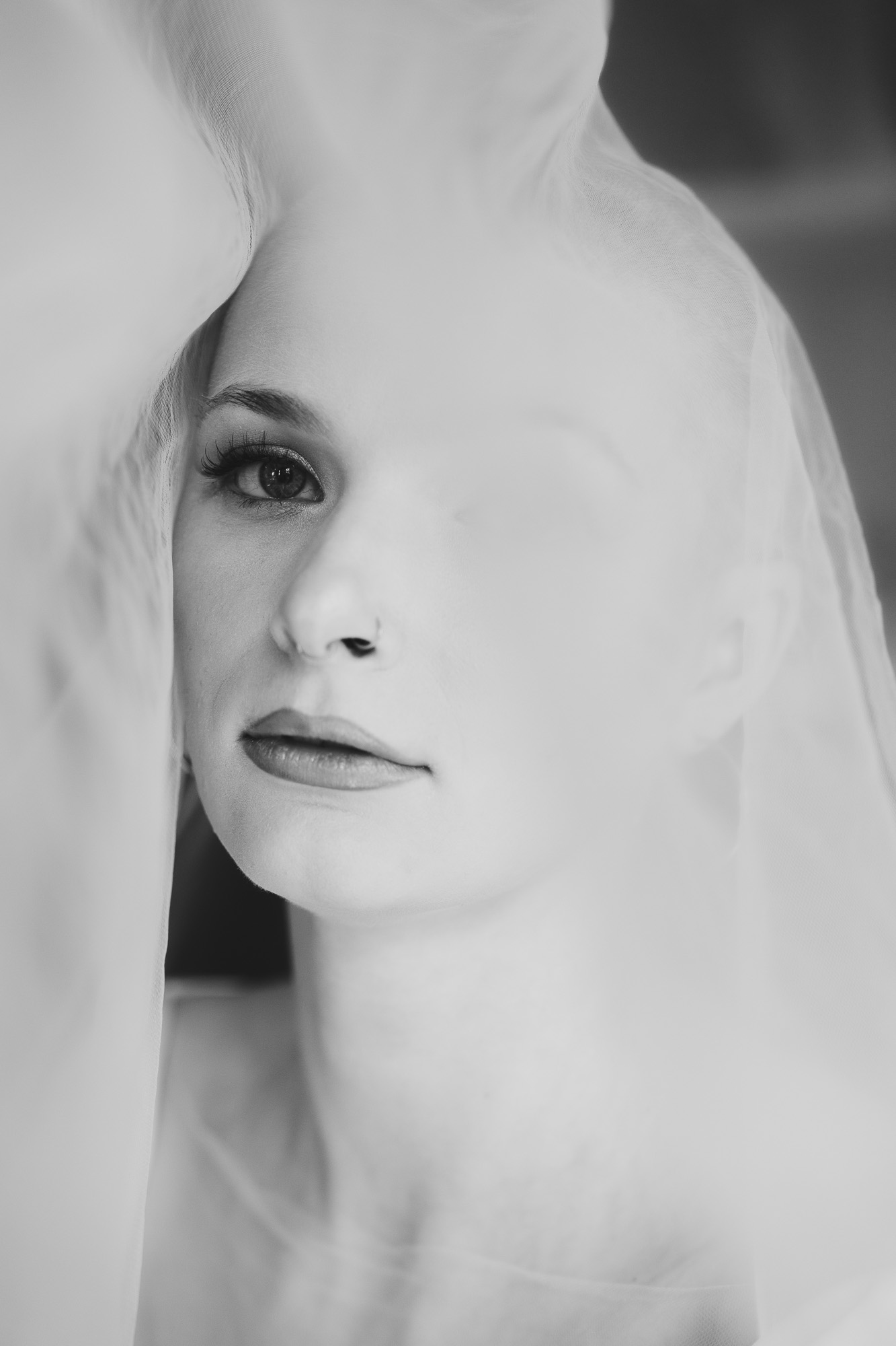 Black-and-white close-up portrait of a woman partially hidden behind translucent fabric.