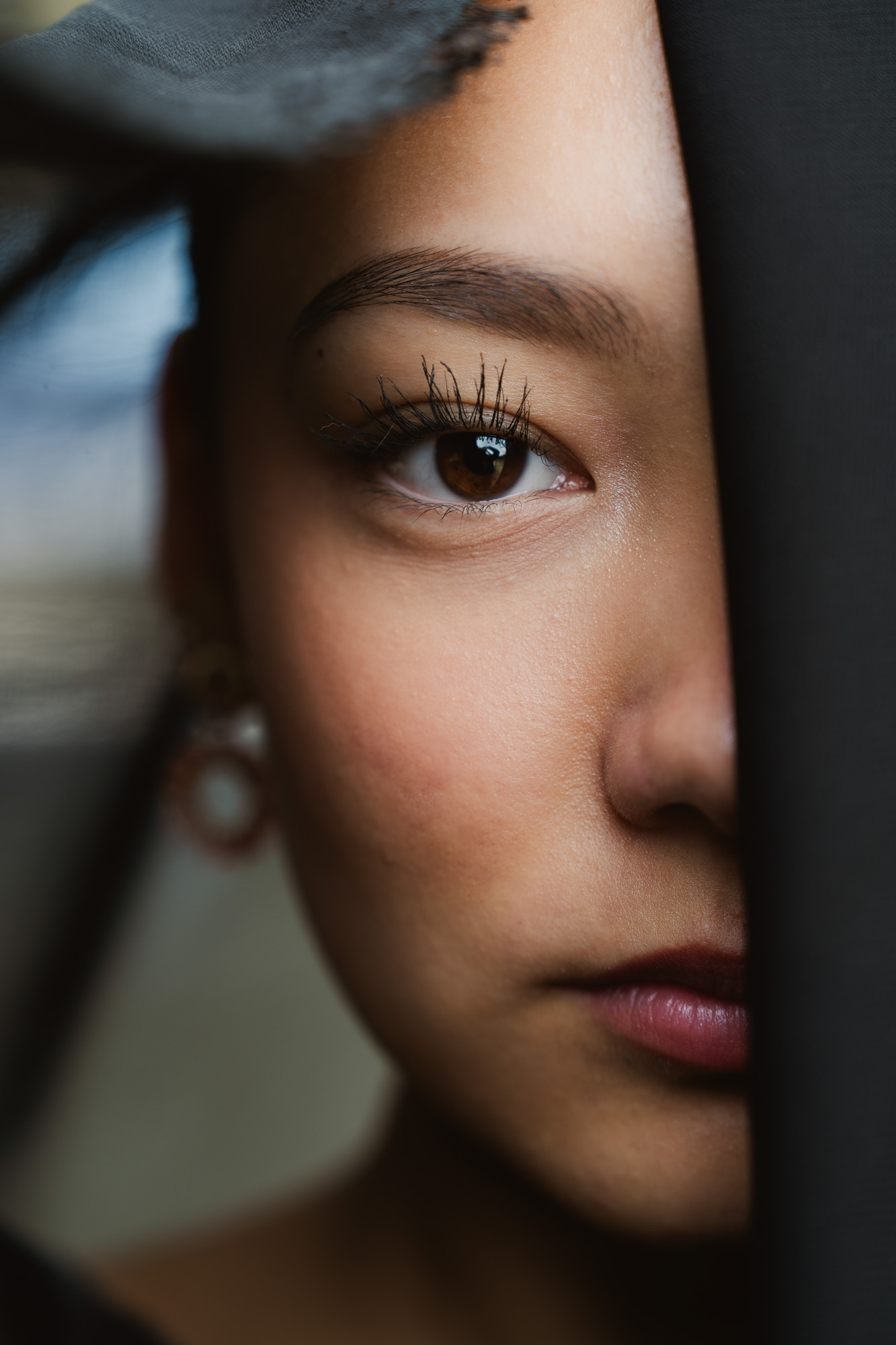 Close-up portrait of a woman framed by deep shadow and translucent fabric.