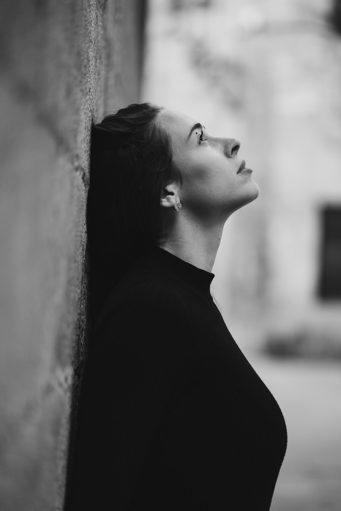 Black-and-white profile portrait of a woman leaning against a wall and looking upward.