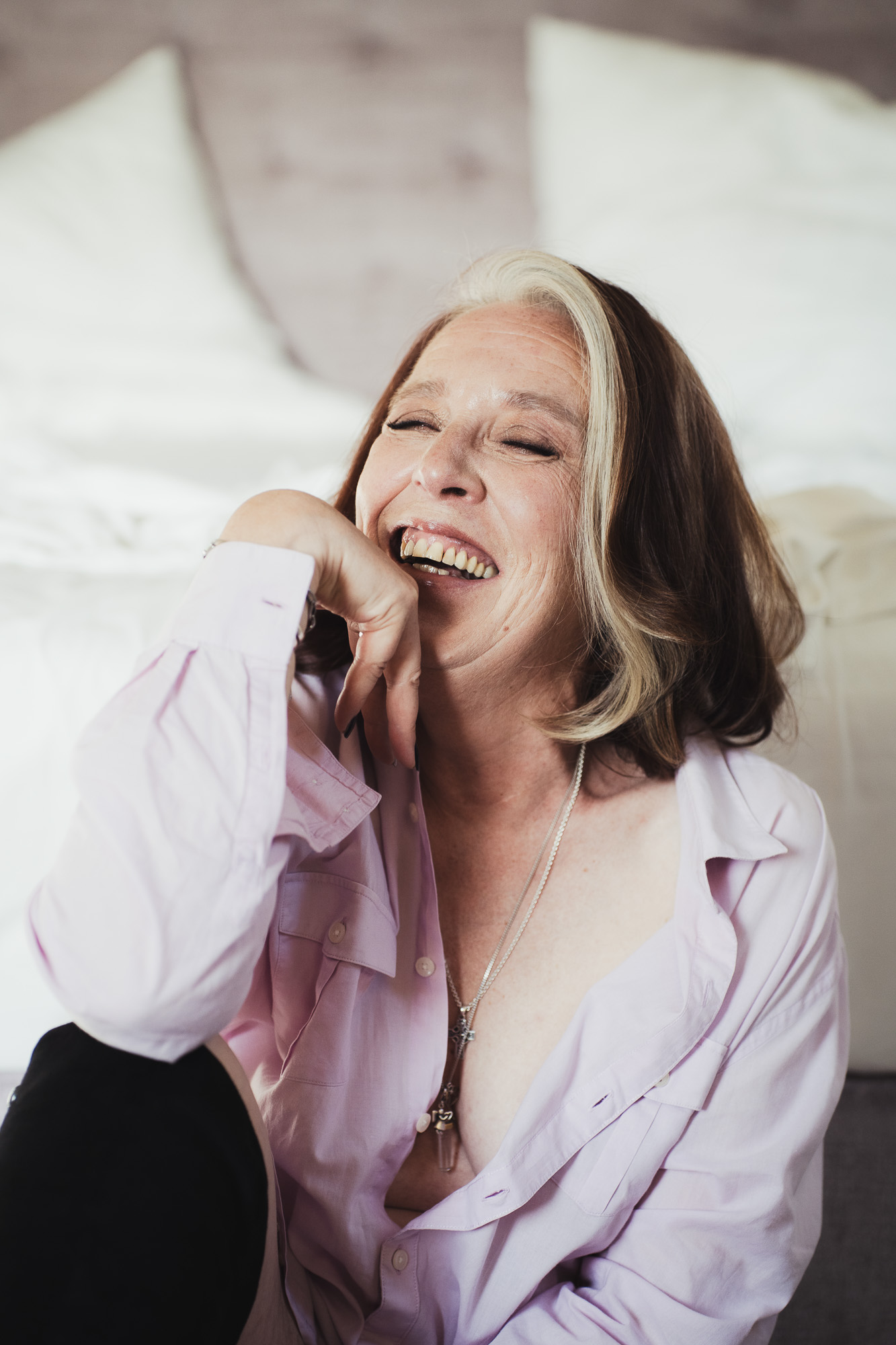 Woman in a lilac shirt laughing during a relaxed portrait session.