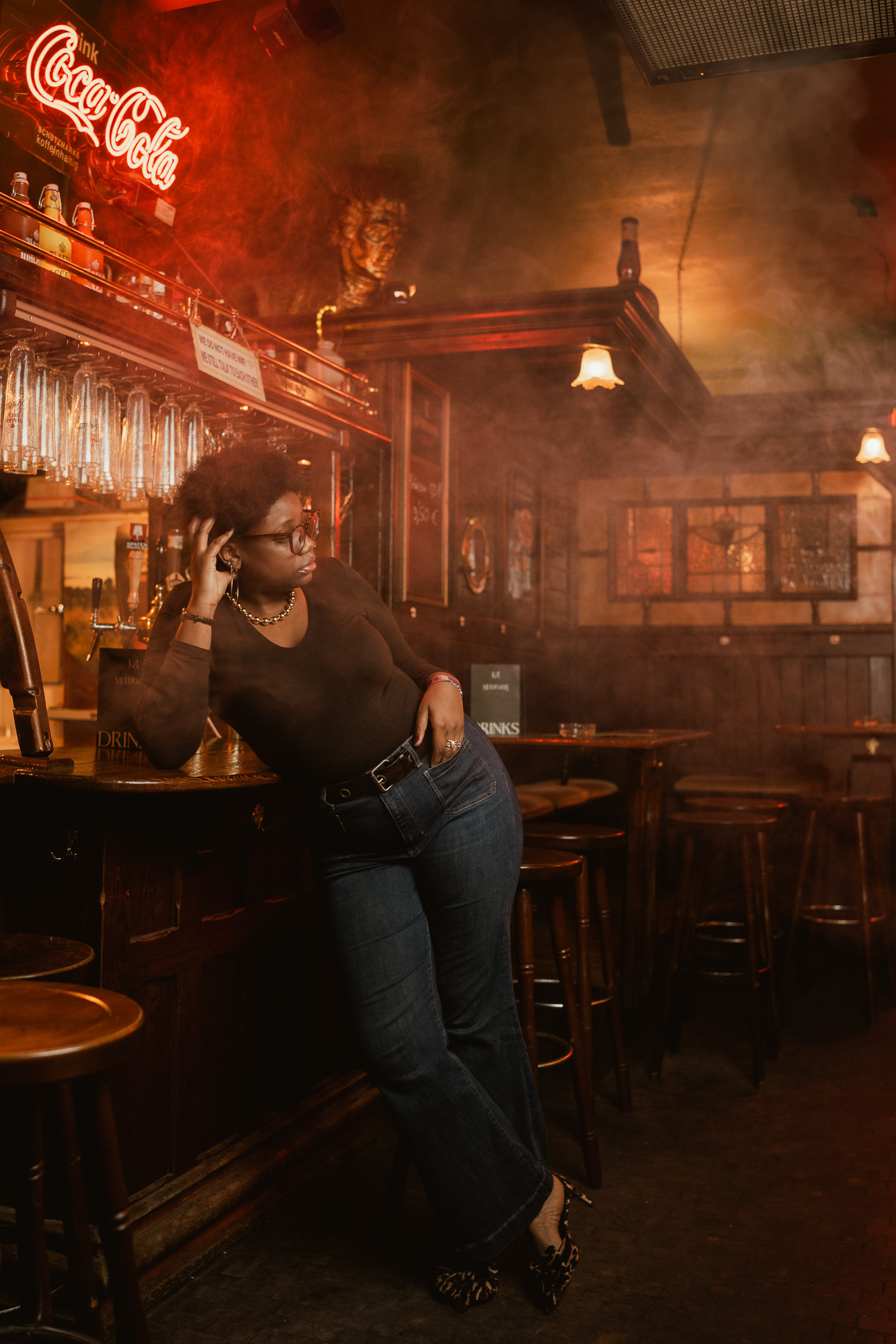 Woman seated in a warmly lit pub surrounded by rich red and amber tones.