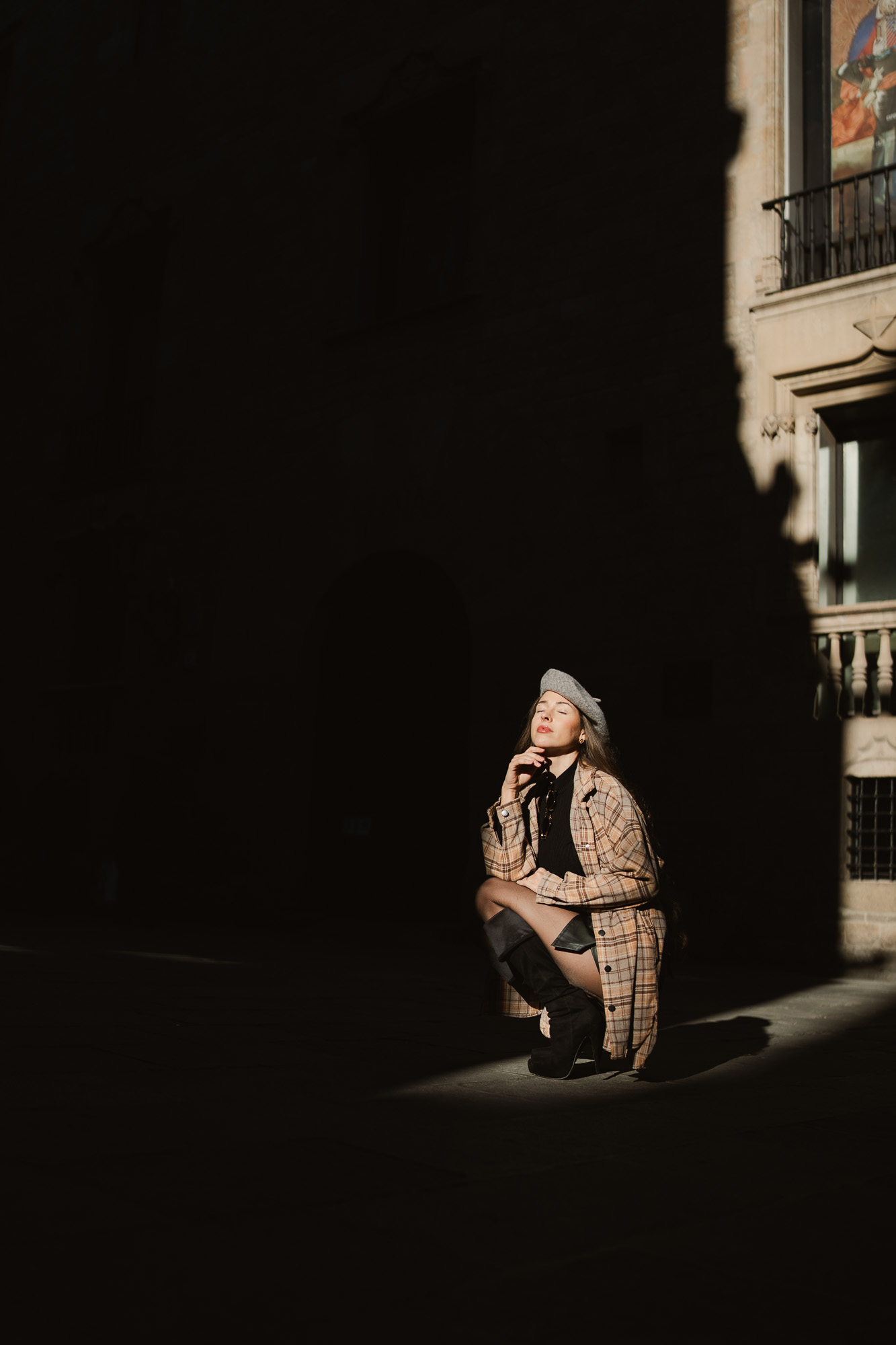 Woman sitting alone in a narrow pool of sunlight against a dark architectural background.