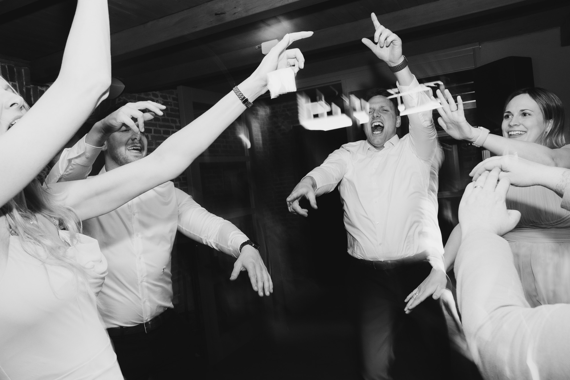 Black-and-white dance floor moment with the groom surrounded by raised hands and wedding guests.