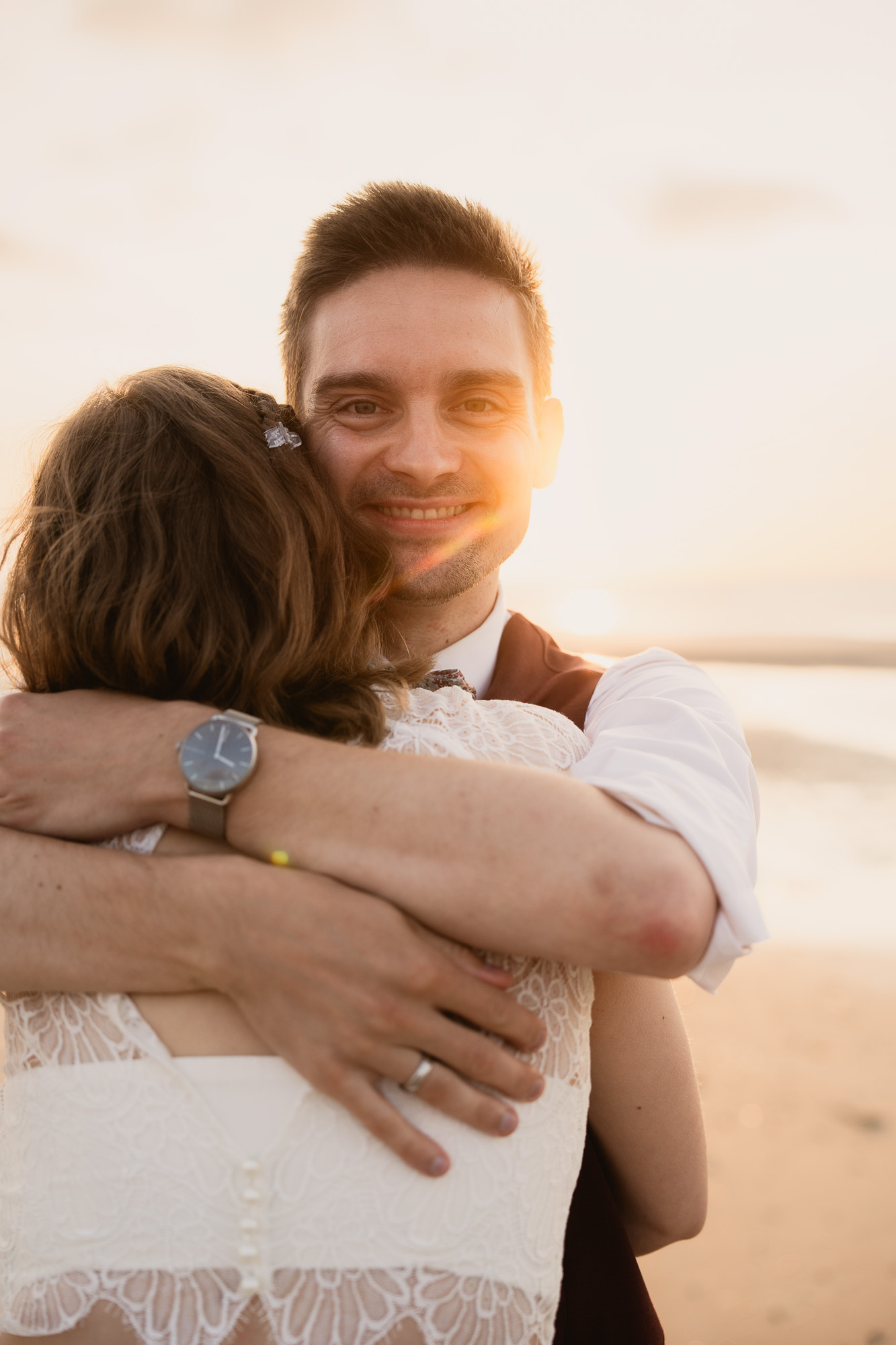 Groom embracing a wedding guest in warm golden evening light.
