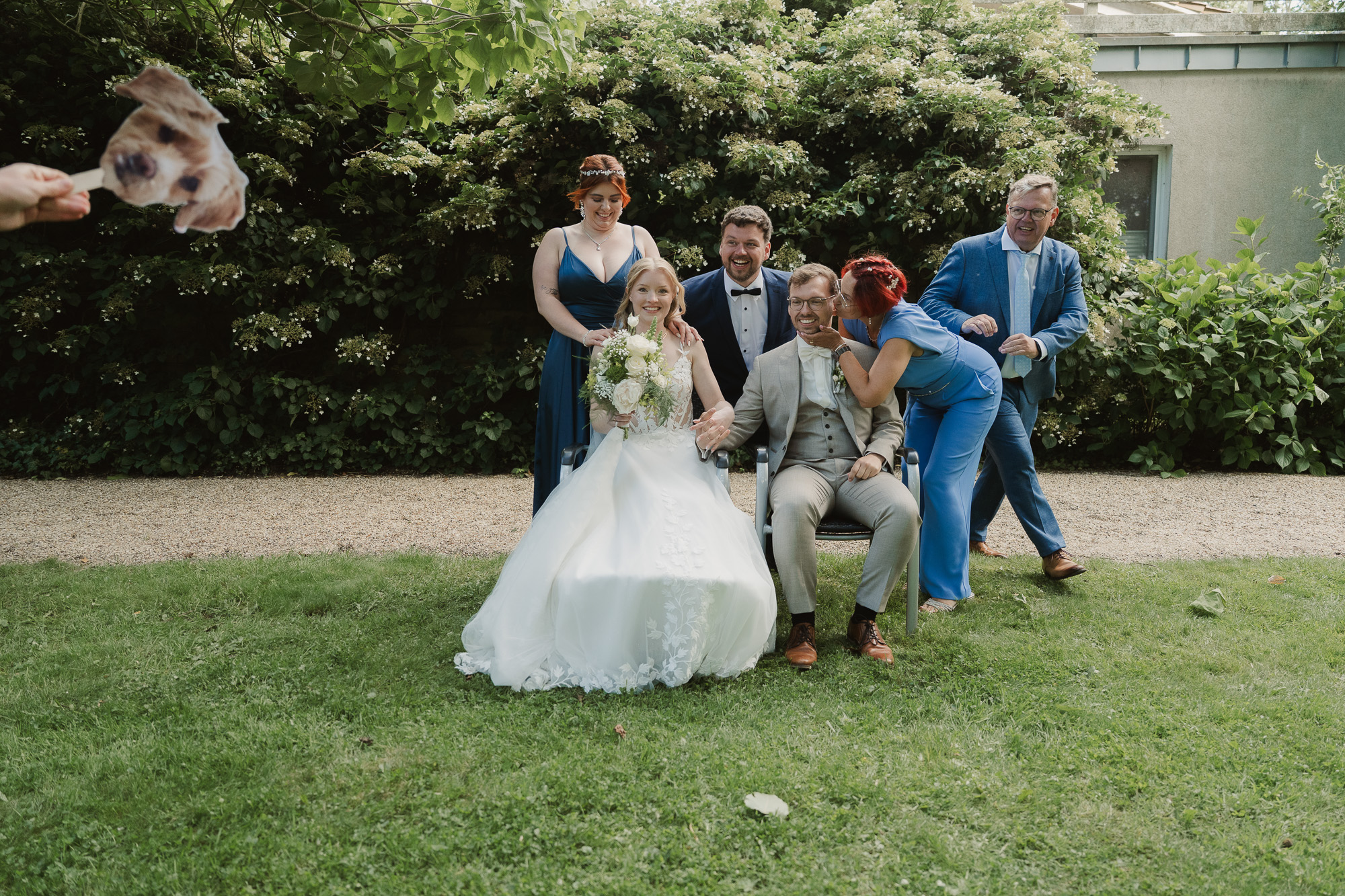 Bride and wedding party posing playfully together on a green lawn.