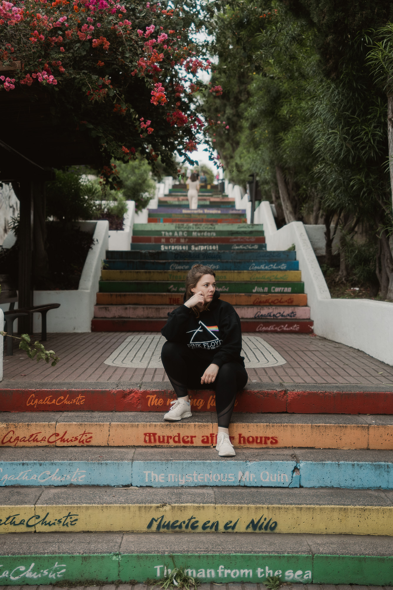Woman sitting on colourful outdoor steps painted with book titles.