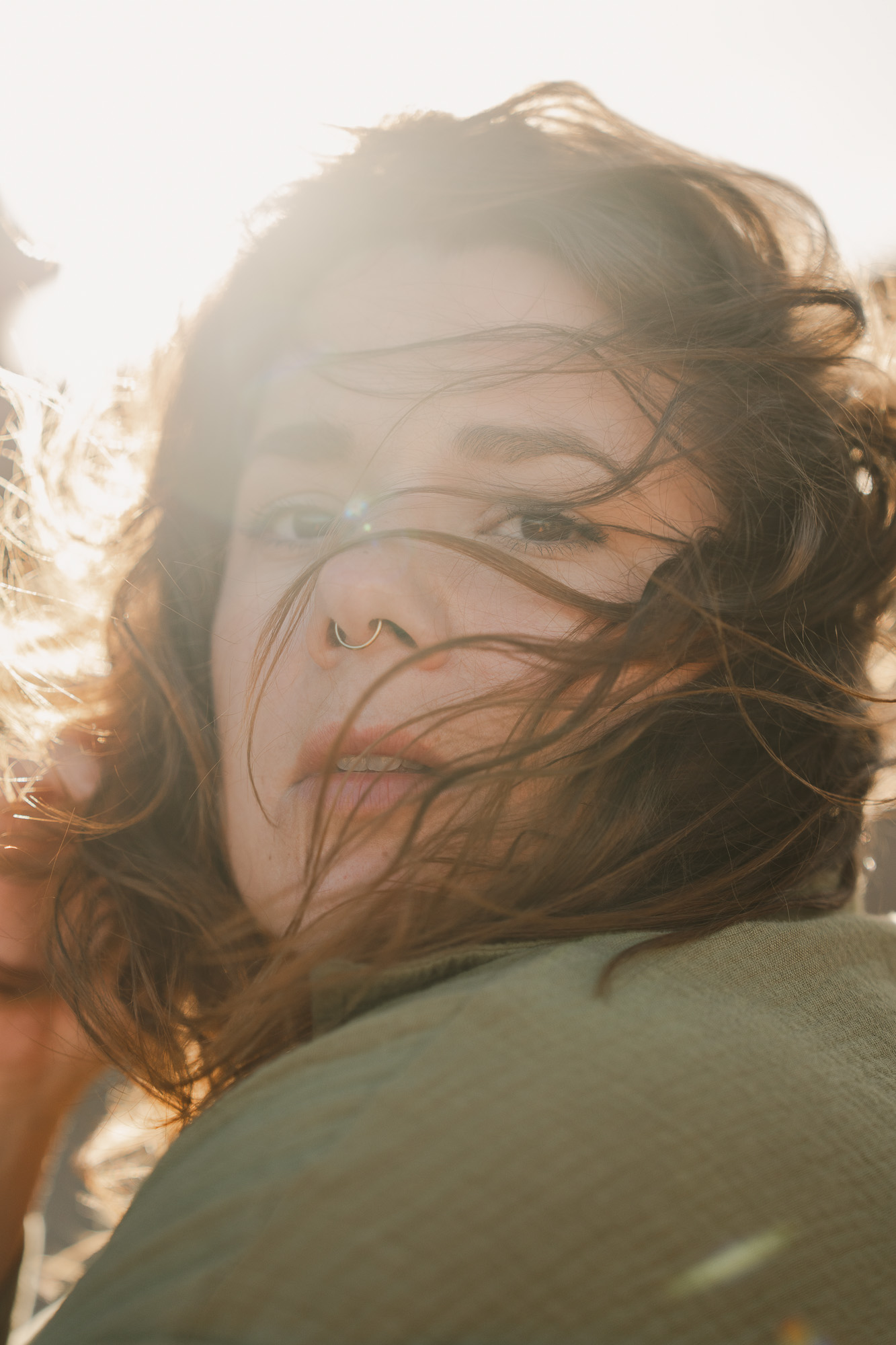 Warm backlit close-up portrait of a woman with wind moving through her hair.