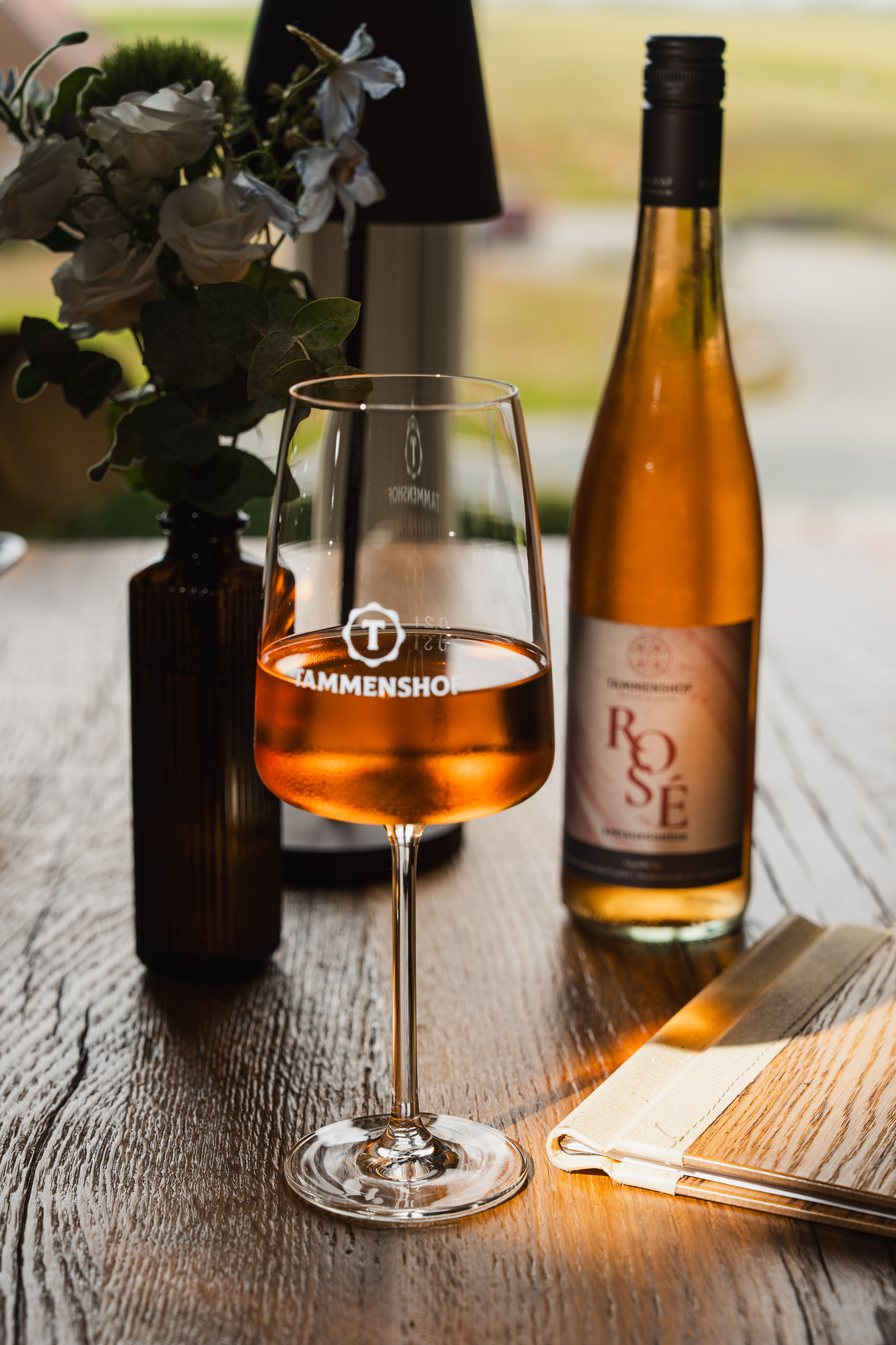 Glass of rosé wine with a bottle and menu beside the restaurant window.