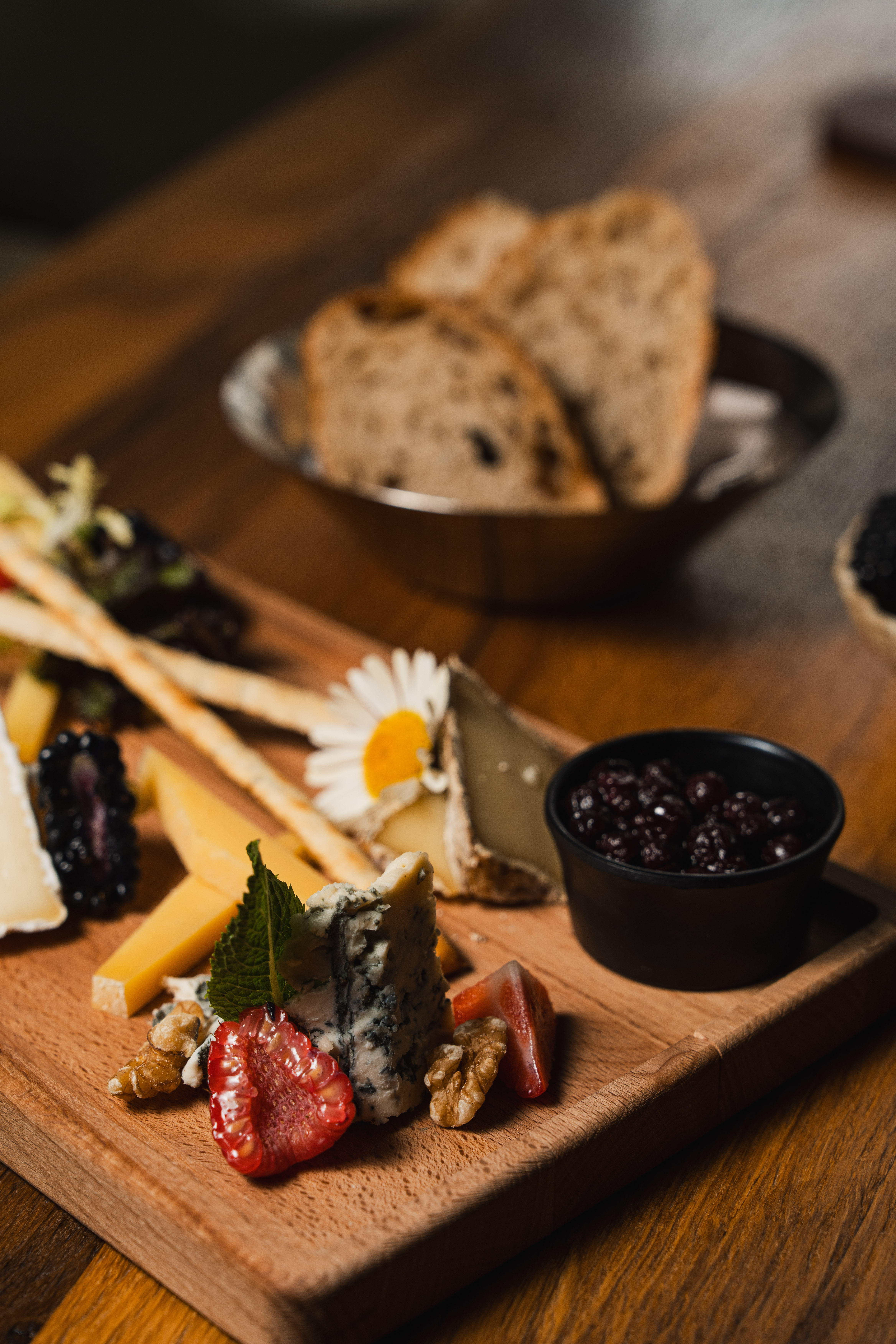Selection of cheeses with berries, bread and edible flowers served on a wooden board.
