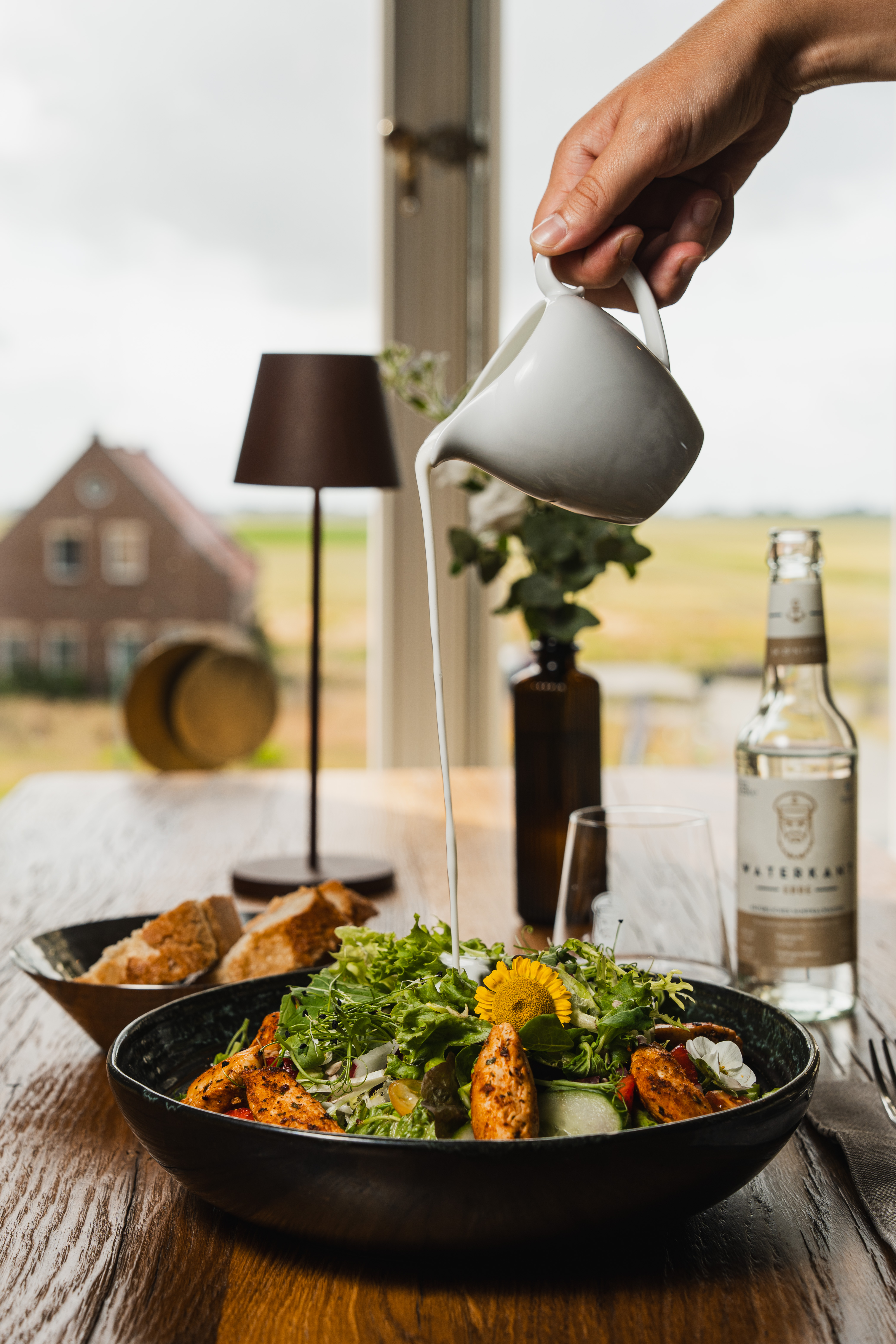 Restaurant employee pouring sauce over a freshly prepared dish in a black bowl.