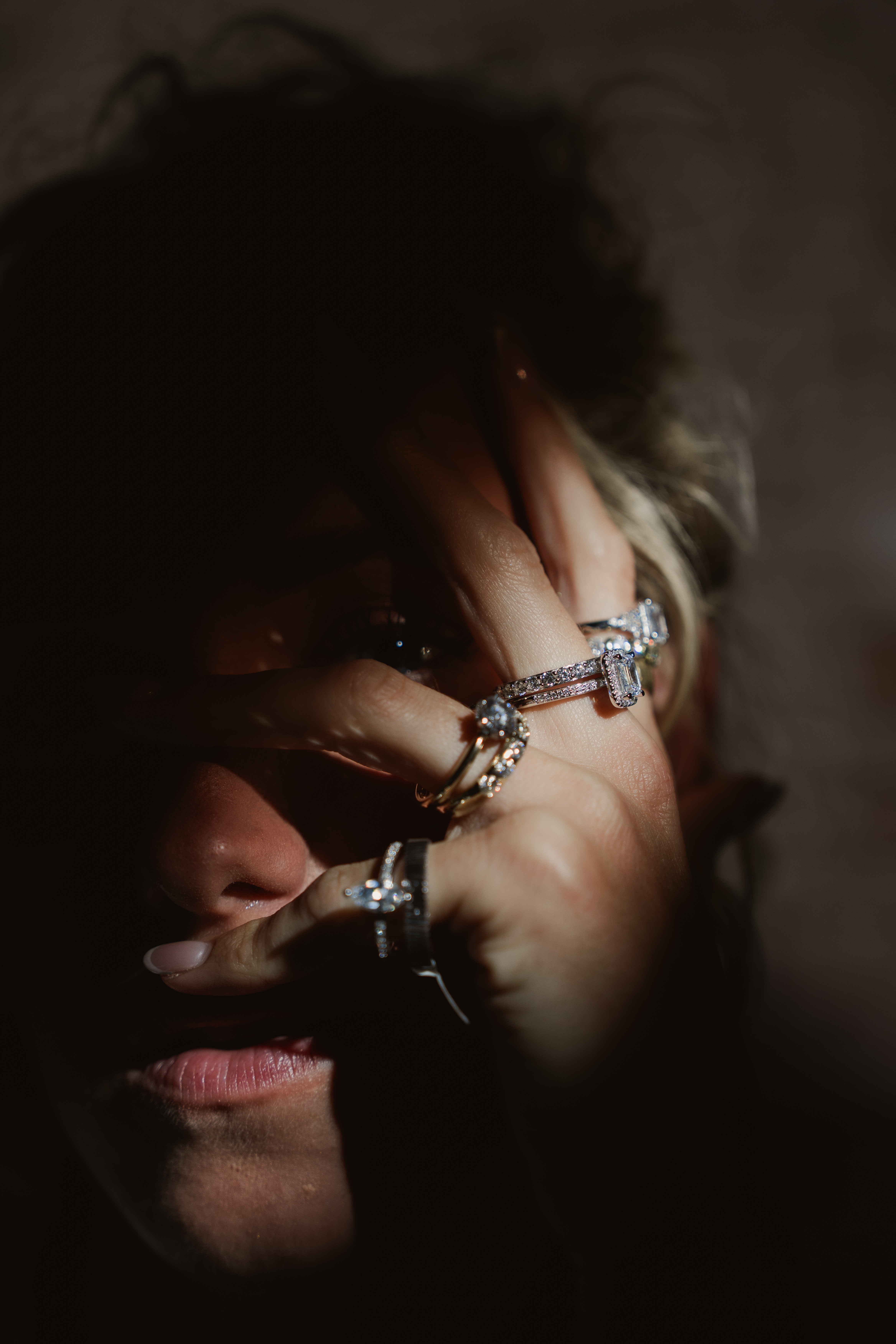Dark editorial portrait with hard shadows and rings positioned across the woman’s face.