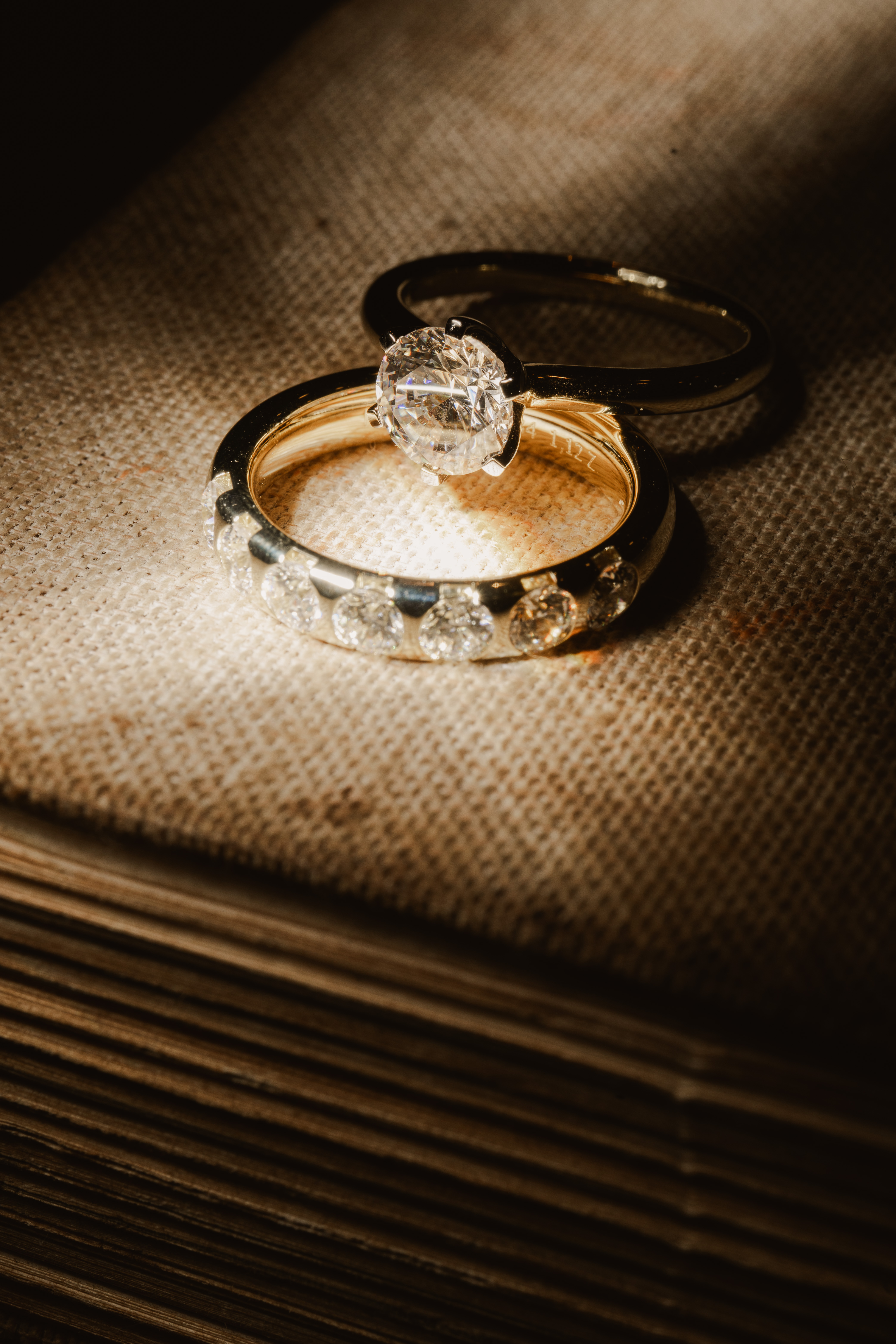 Two rings with gemstones arranged on a textured neutral surface in warm directional light.