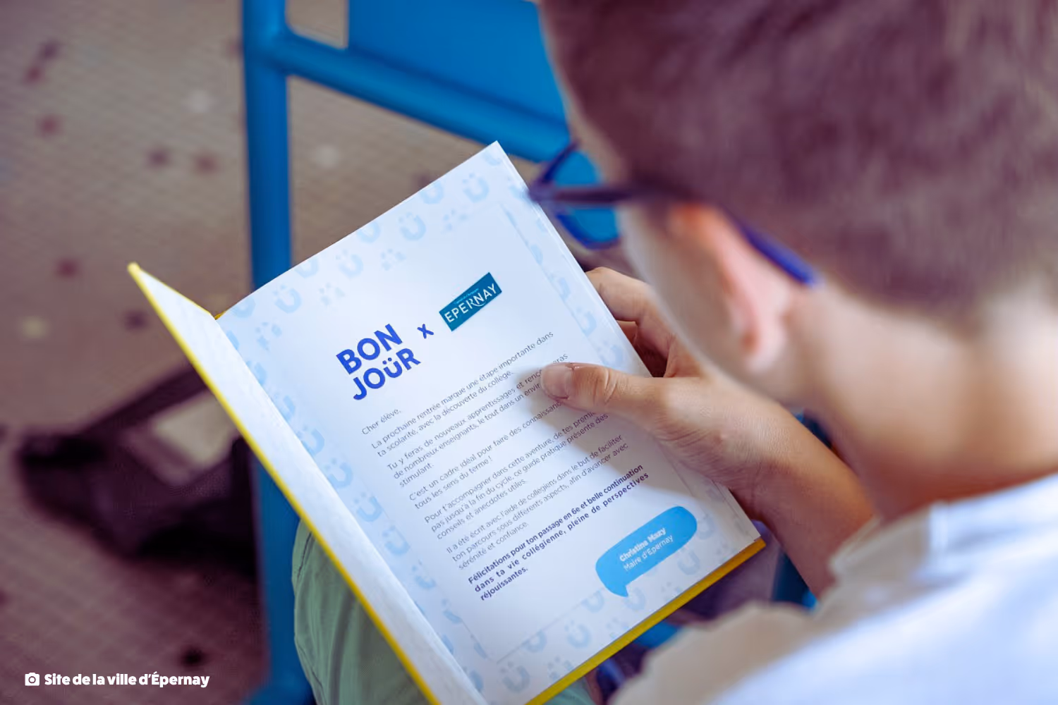 Élève tenant une brochure intitulée BONJOUR x EPERNAY avec un message de bienvenue pour la rentrée scolaire.
