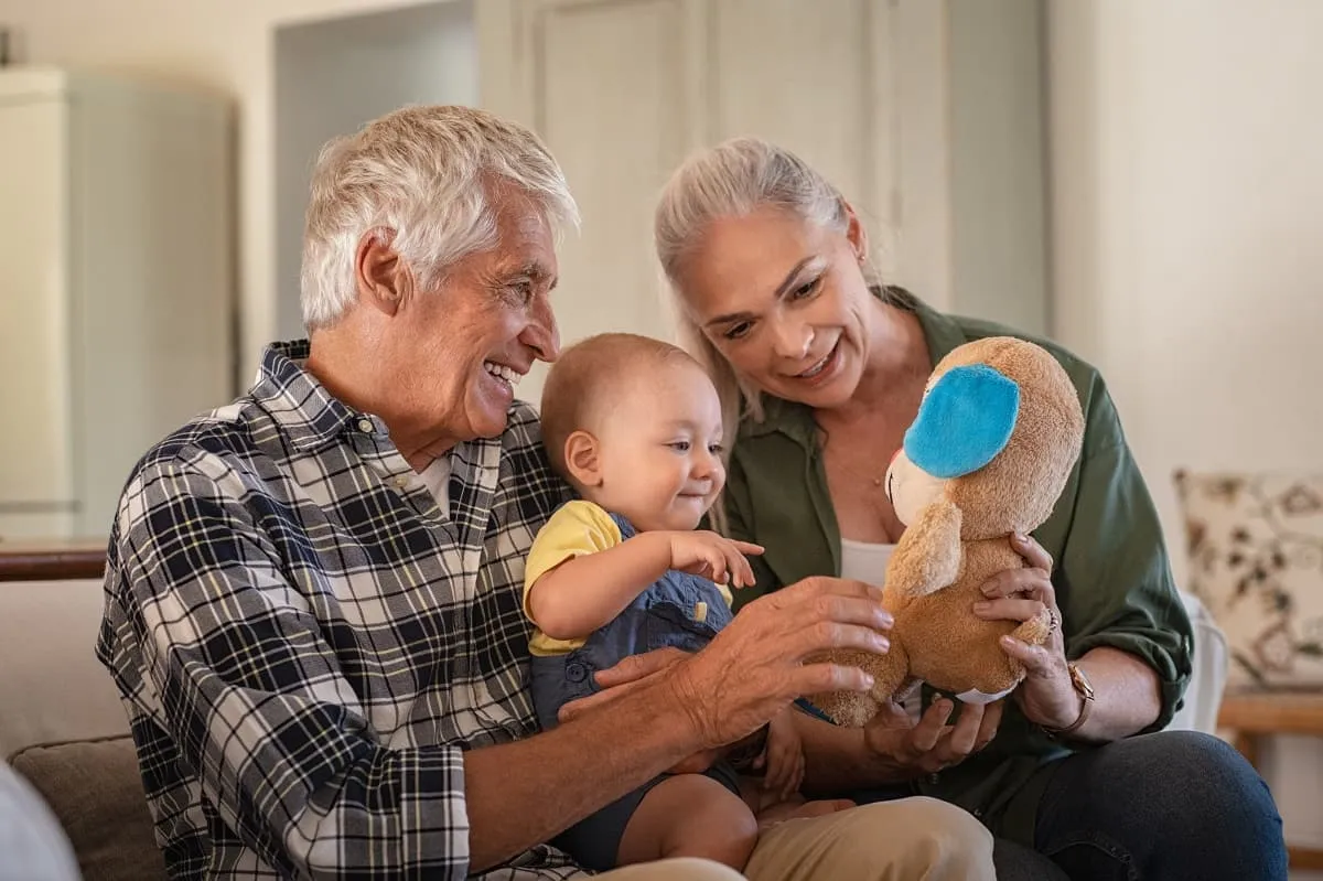 Grandparents sitting with their grandson playing with a stuffed dog toy at home.