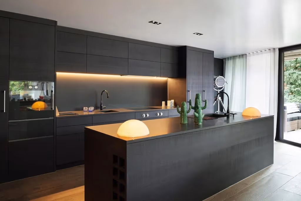Luxury dark kitchen with matte black cabinets, large island, integrated appliances and warm under-cabinet lighting in an open-plan space