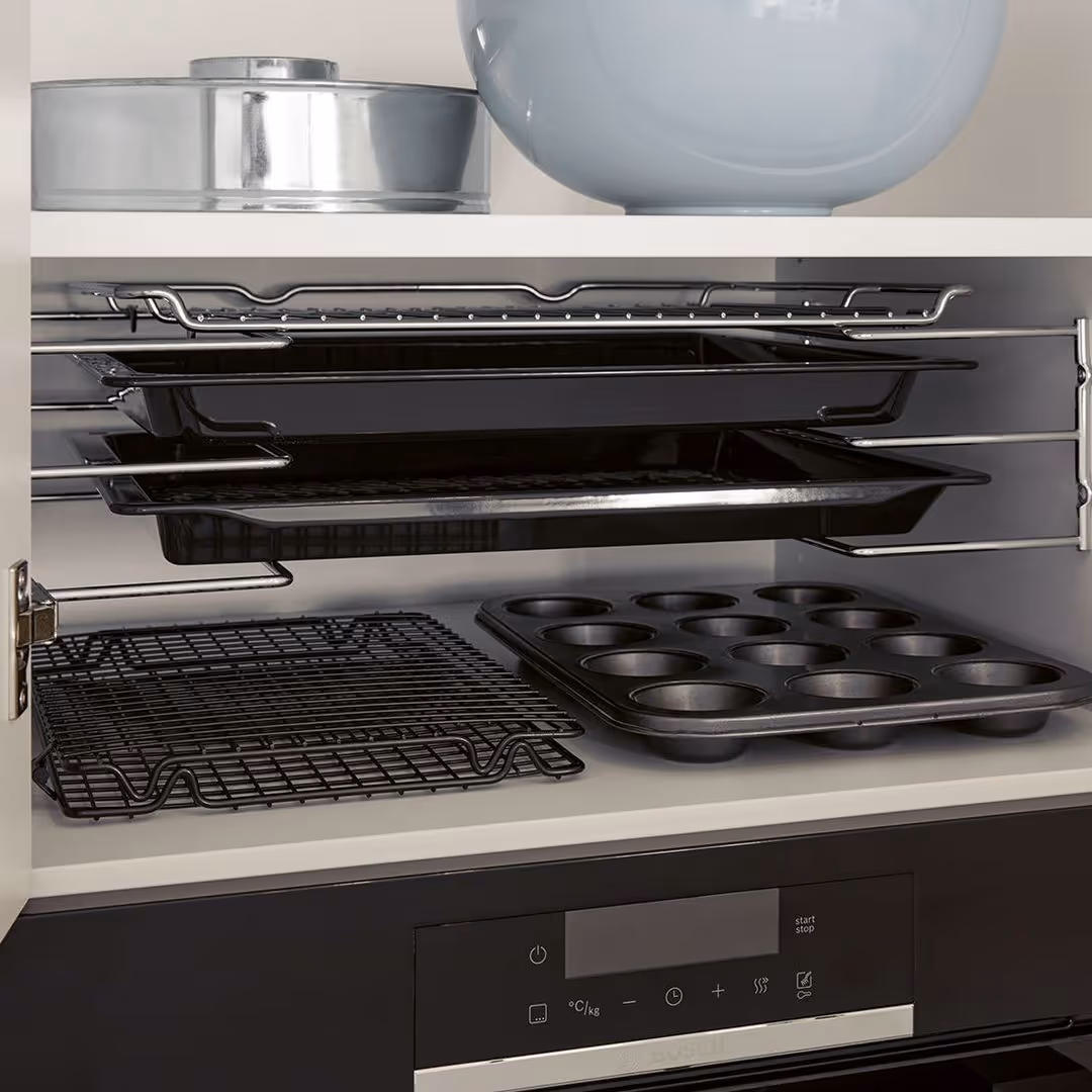 Open kitchen cabinet showing various baking trays and pans neatly organized inside.