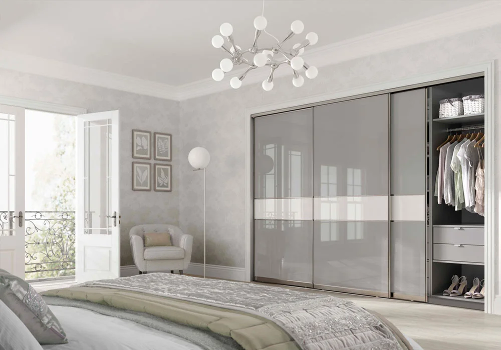 A bedroom with a sliding wardrobe partly open, revealing hanging clothes and drawers. A bed and chair nearby.