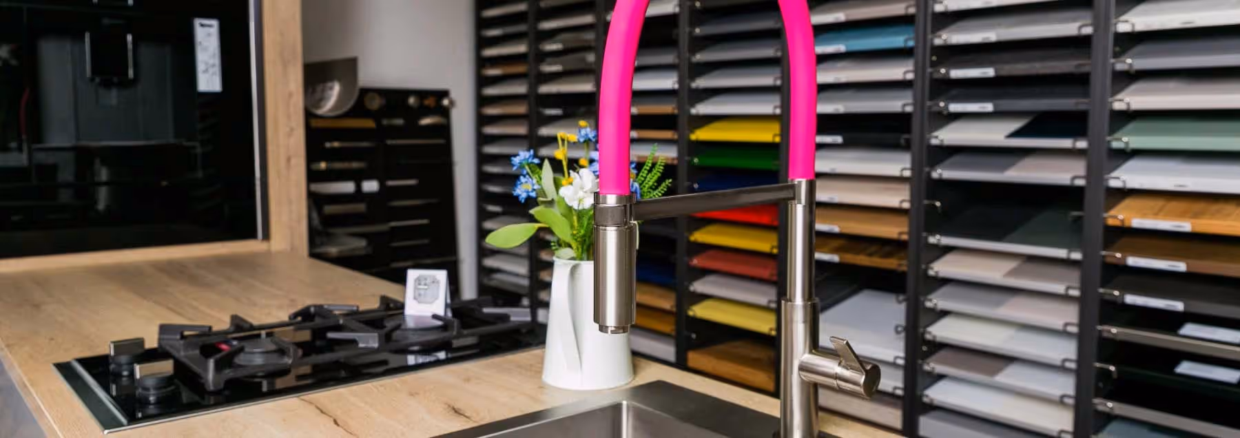 A kitchen countertop with a sink and a pink faucet, and a vase of flowers beside it.