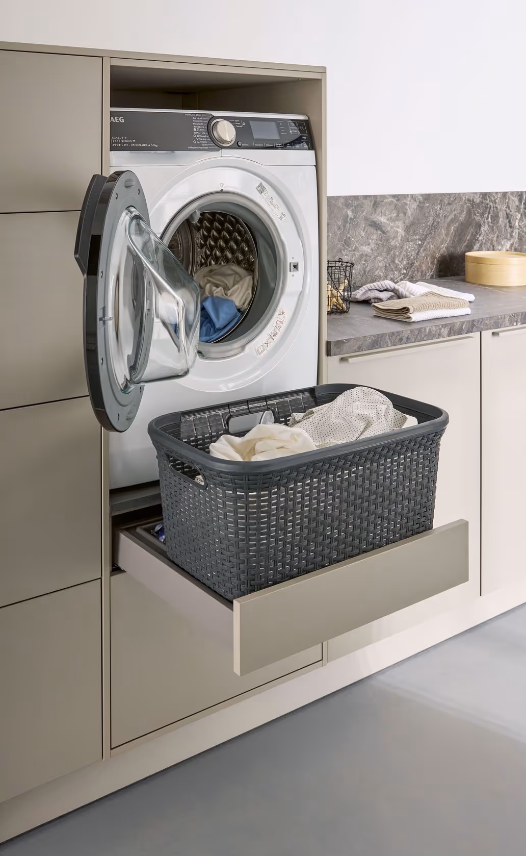 A washing machine has its door open with a laundry basket on a pull-out tray.