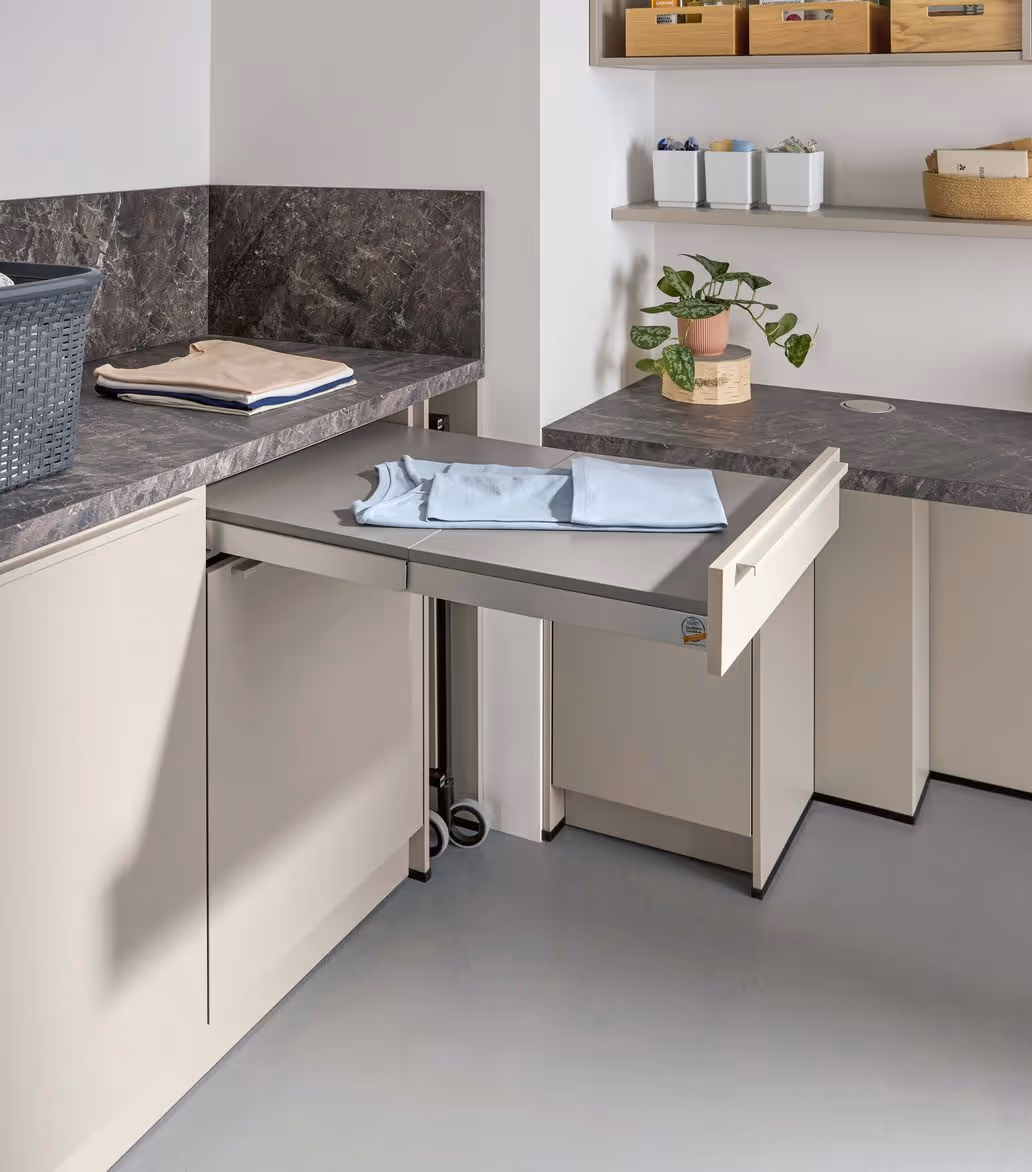 A folded ironing board extends from a cabinet in a laundry room with a few folded clothes.