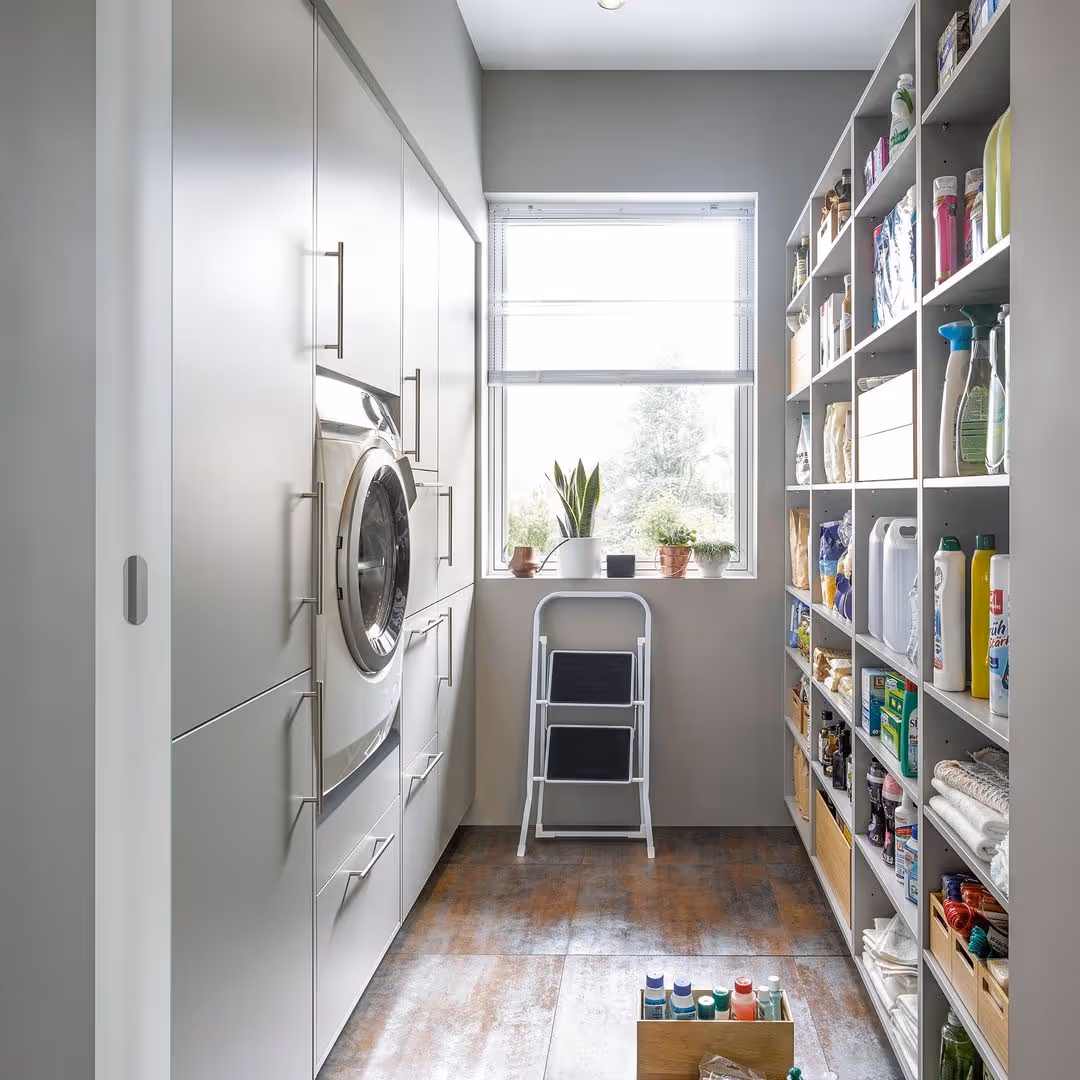 Laundry room with stacked washer and dryer, shelves filled with supplies, and a small step ladder.