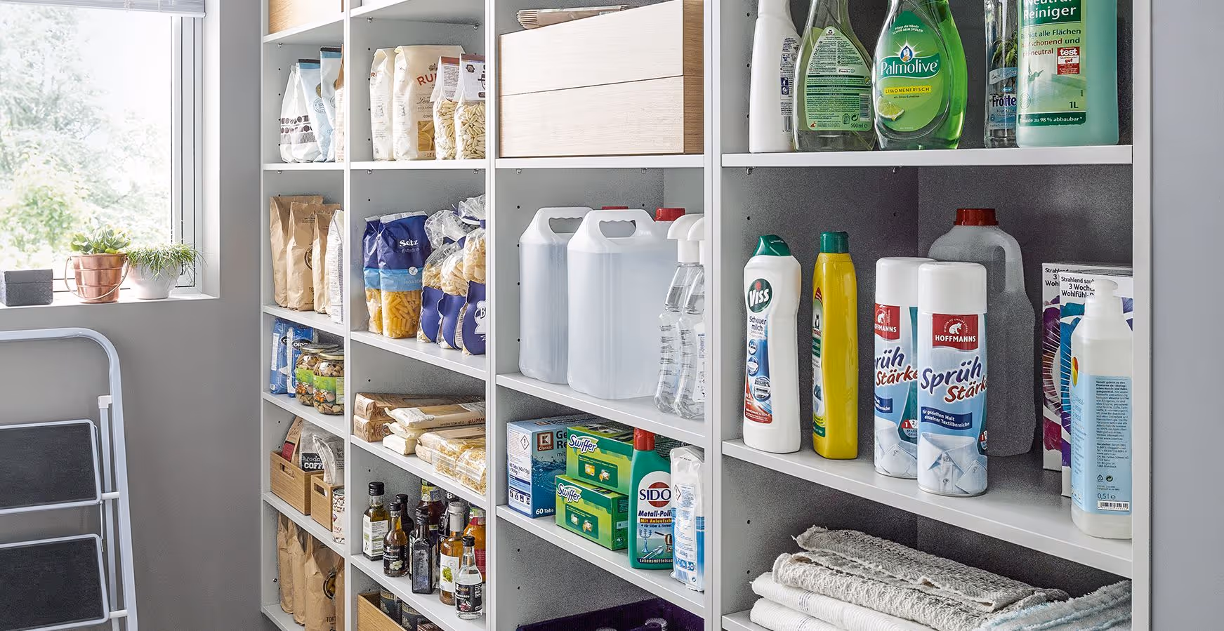 Shelves are filled with household cleaning products, food items, and folded towels in a storage area.