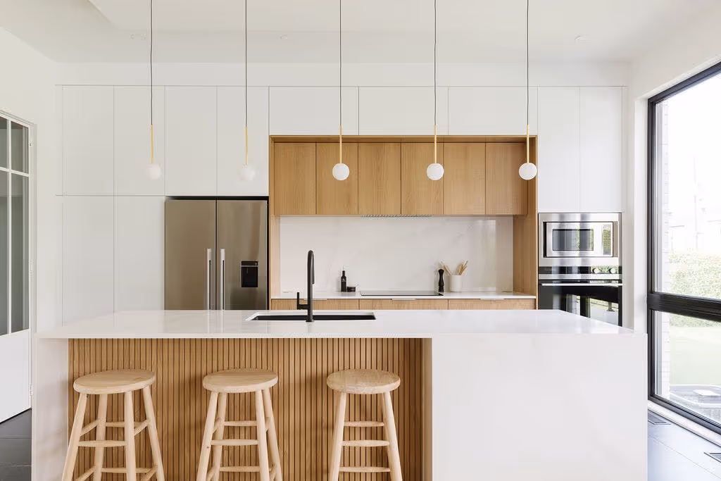 Modern kitchen with a large island, three wooden stools, and hanging pendant lights above the counter.