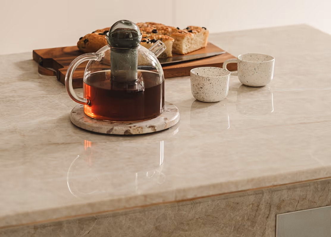 A teapot with tea infuser and two mugs on a counter, next to sliced bread.