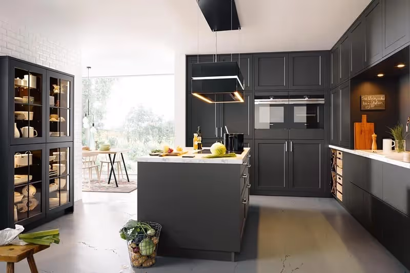 Modern kitchen with dark cabinets, center island, and hanging lights. Various vegetables placed on the island.